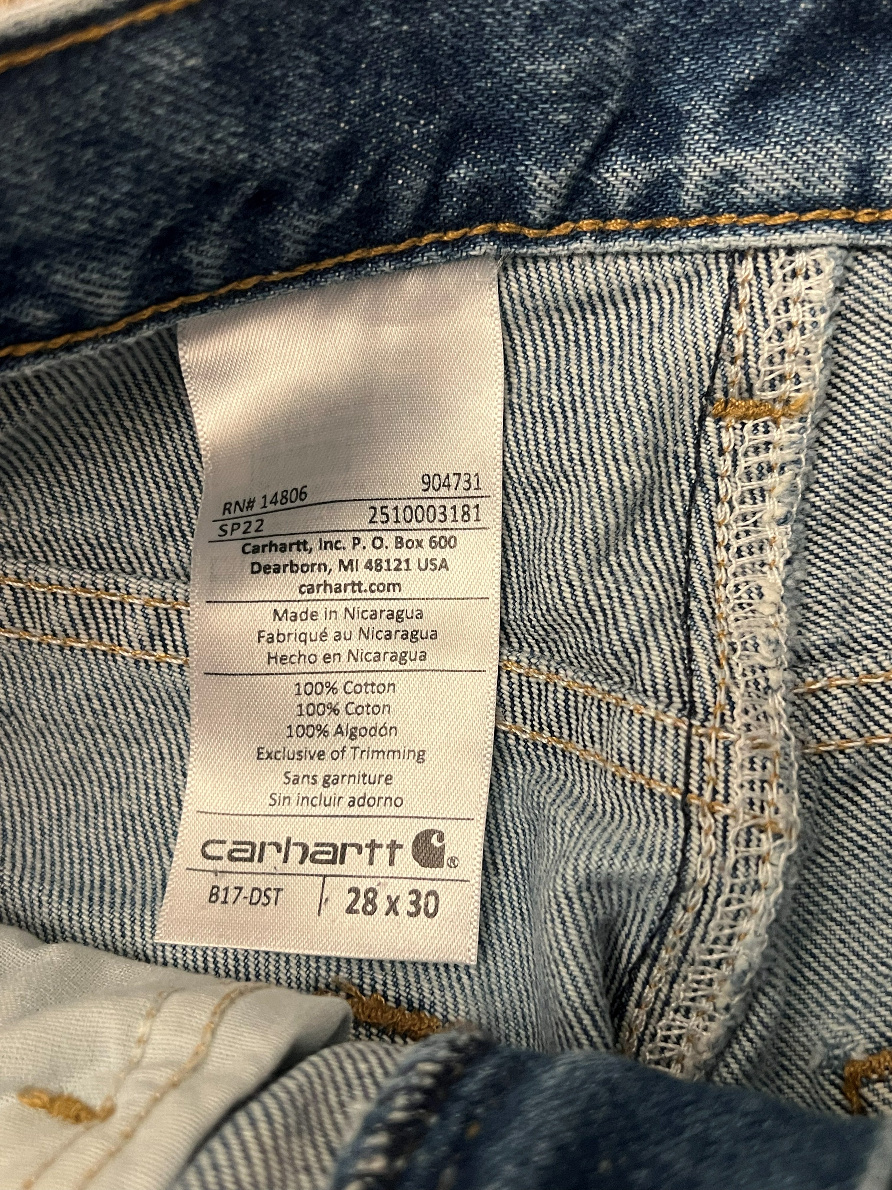 Close-up of the inside waistband of a pair of blue denim jeans, showing the sewn-on Carhartt brand label with size 28 x 30.