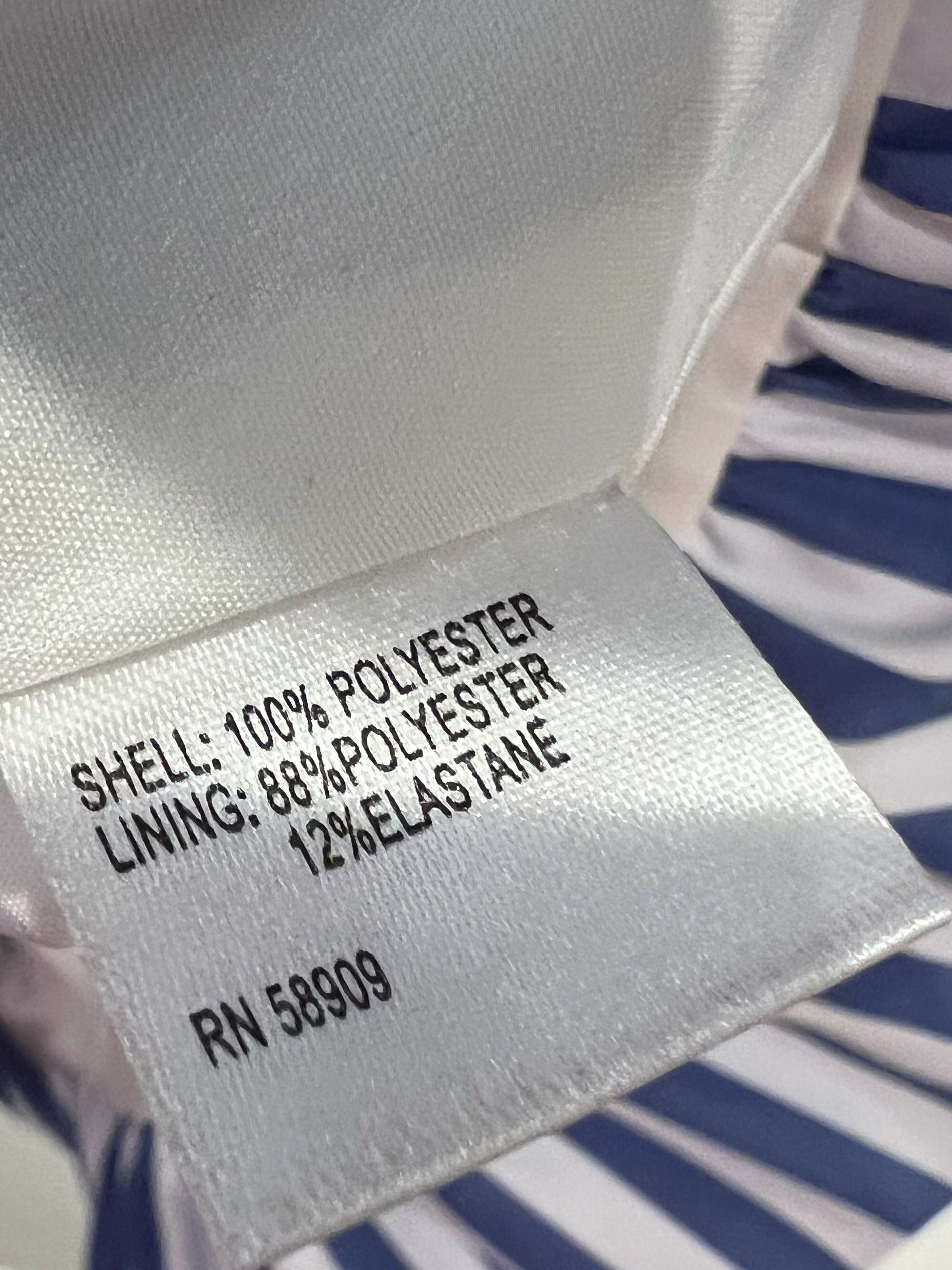 Close-up of a garment's interior label reading 'SHELL: 100% POLYESTER LINING: 68% POLYESTER 12% ELASTANE' with a blue and white striped fabric visible around it.