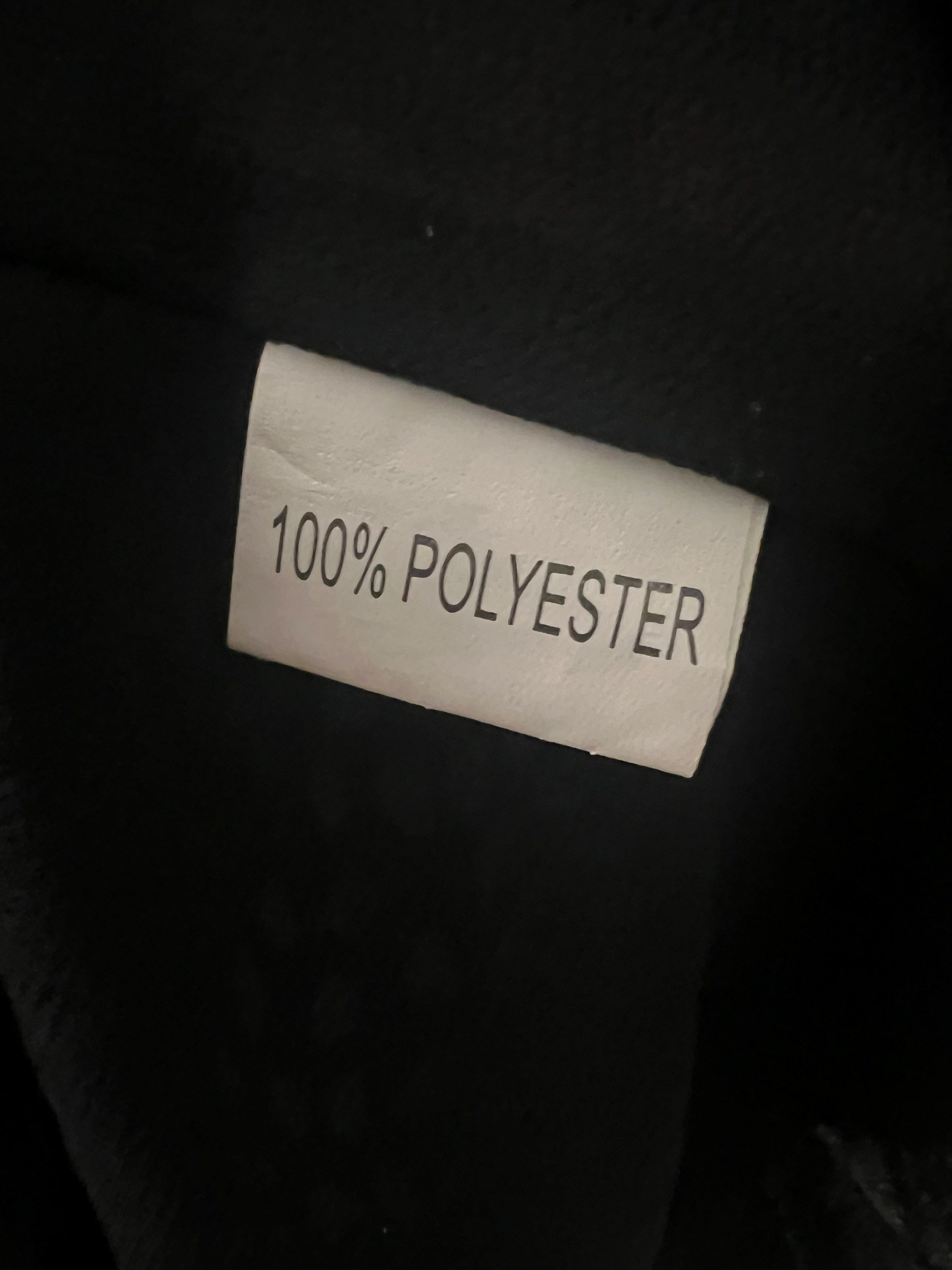 A close-up of a black garment with a sewn-on white fabric label that reads '100% POLYESTER'.