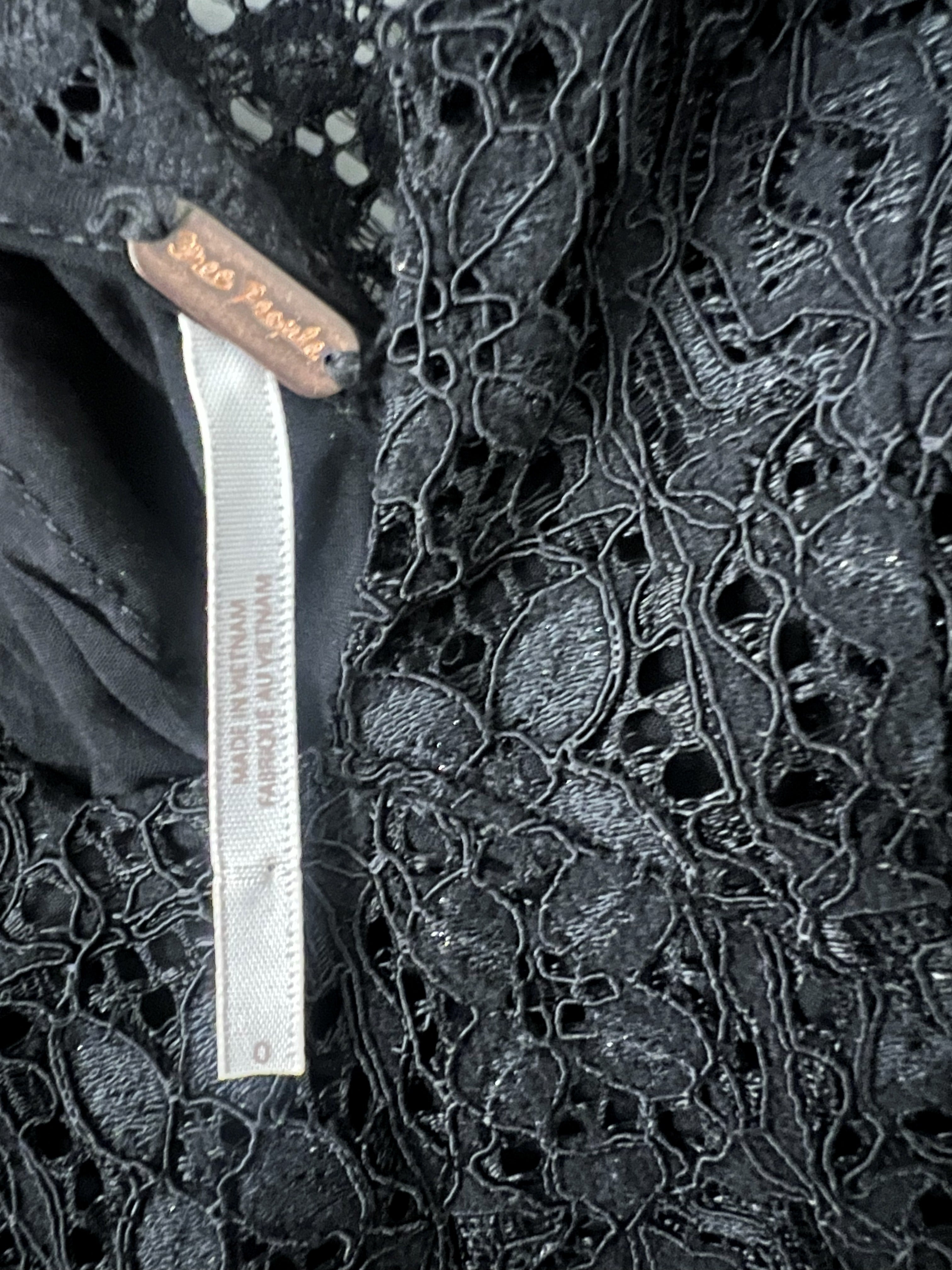 Close-up of a black lace garment with a visible white fabric tag and a small brown label reading Free People.