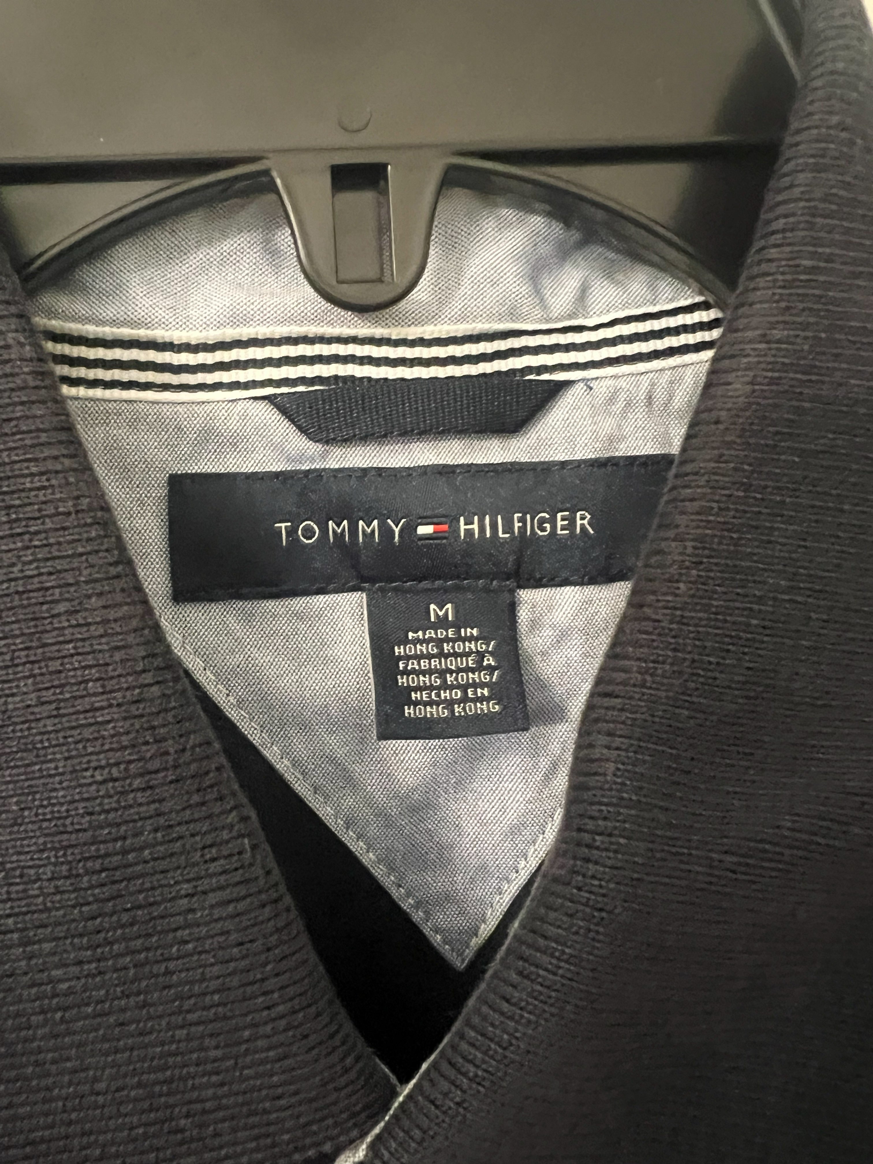 Close-up of a Tommy Hilfiger knit garment collar showing the black brand label, size tag, striped inner neck lining, and dark ribbed fabric.