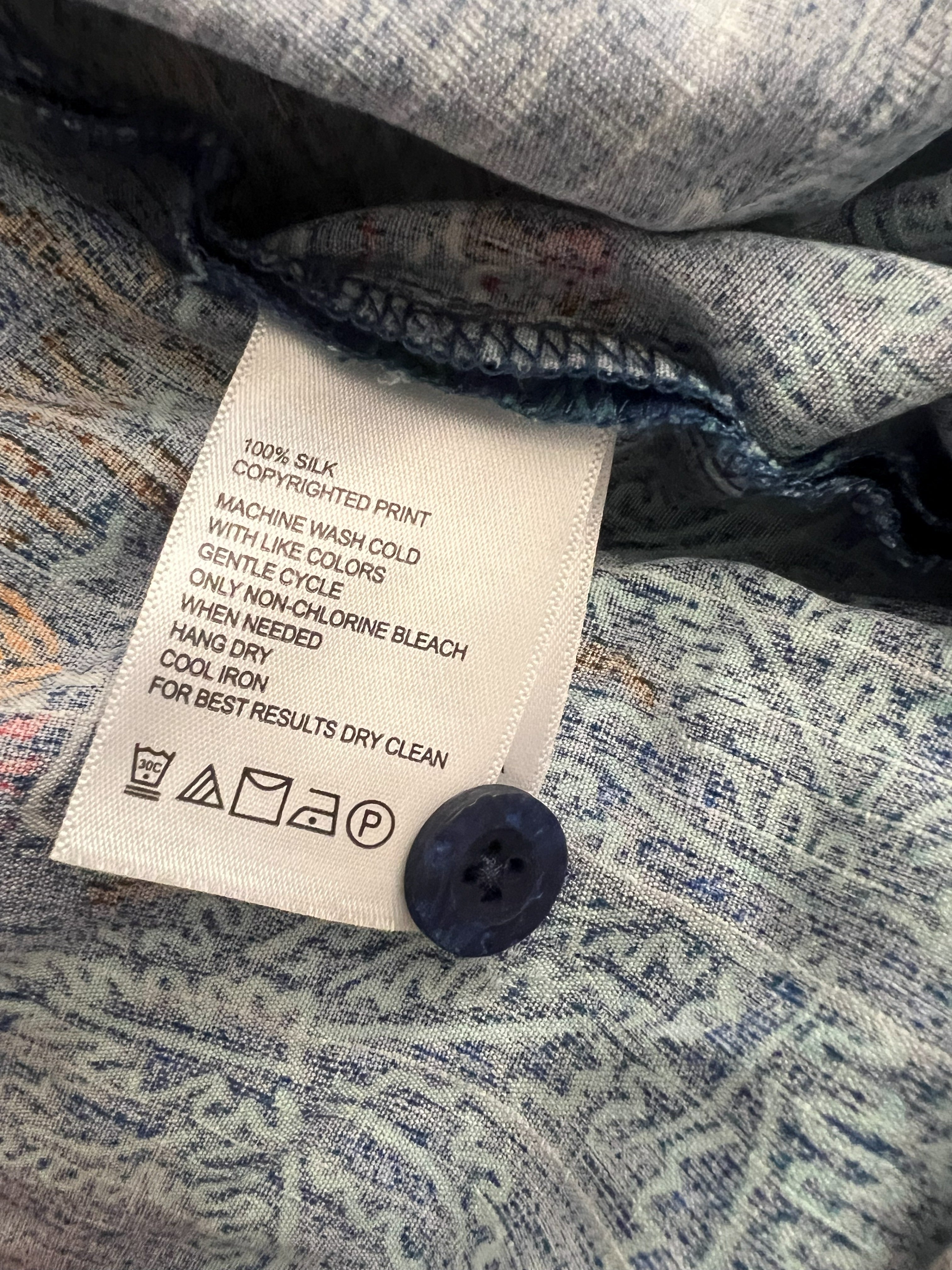 Close-up of a clothing label sewn onto patterned blue and white fabric, with a dark blue button nearby.