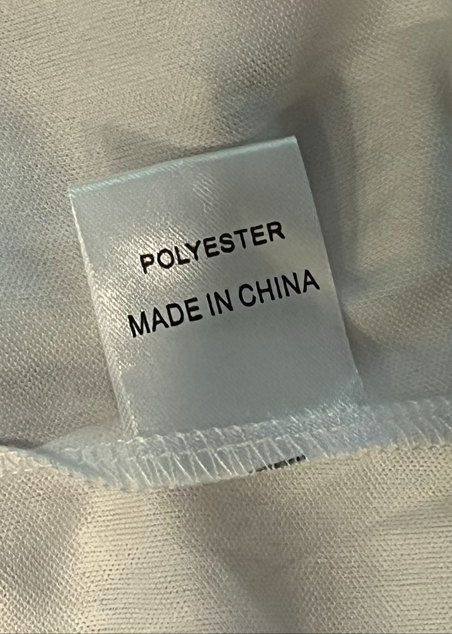 Close-up of a fabric tag reading 'POLYESTER MADE IN CHINA' sewn onto light beige woven clothing.