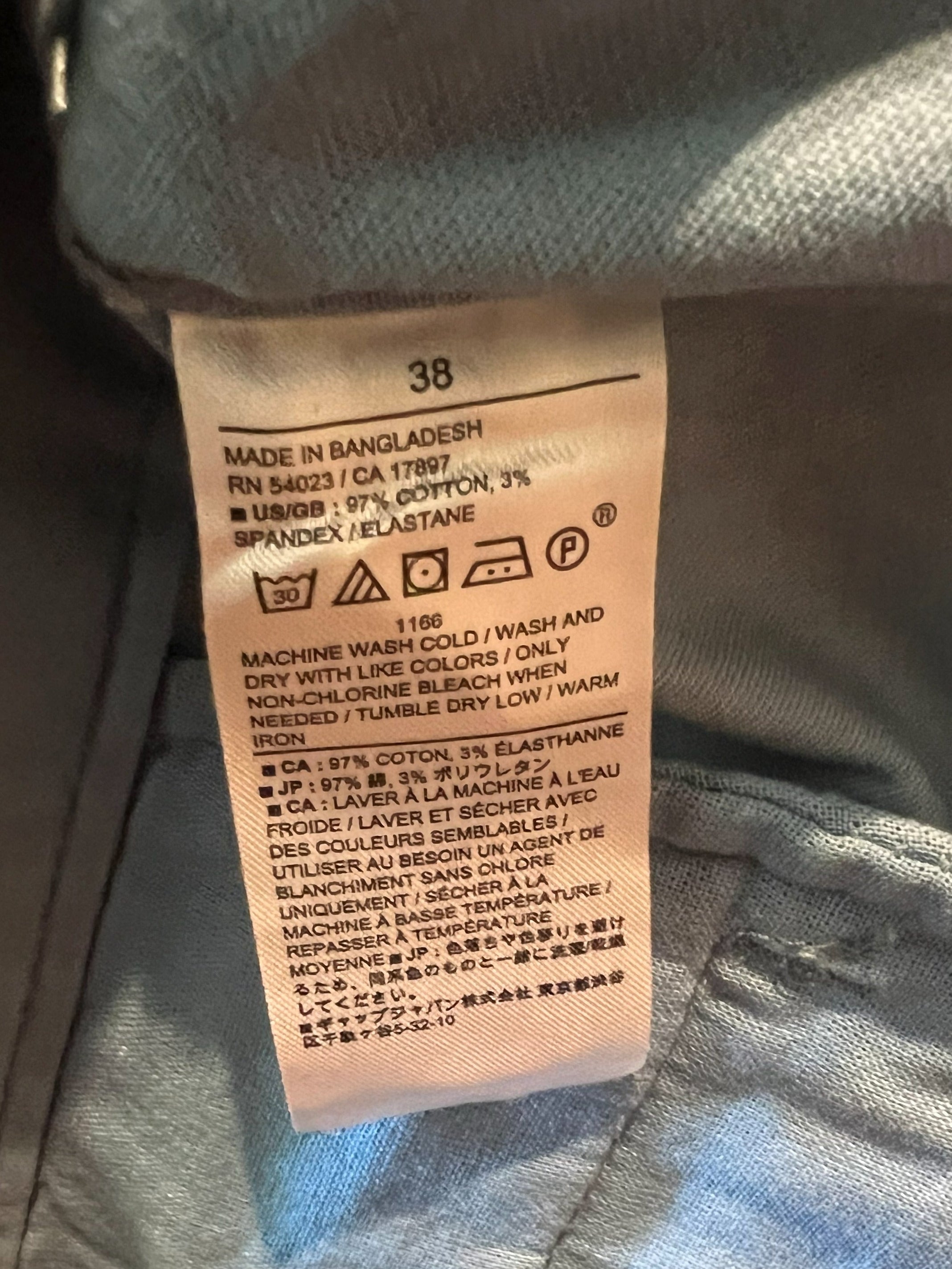 Close-up of a garment's interior label showing size 38 and care instructions, with light blue-gray fabric surrounding the tag.