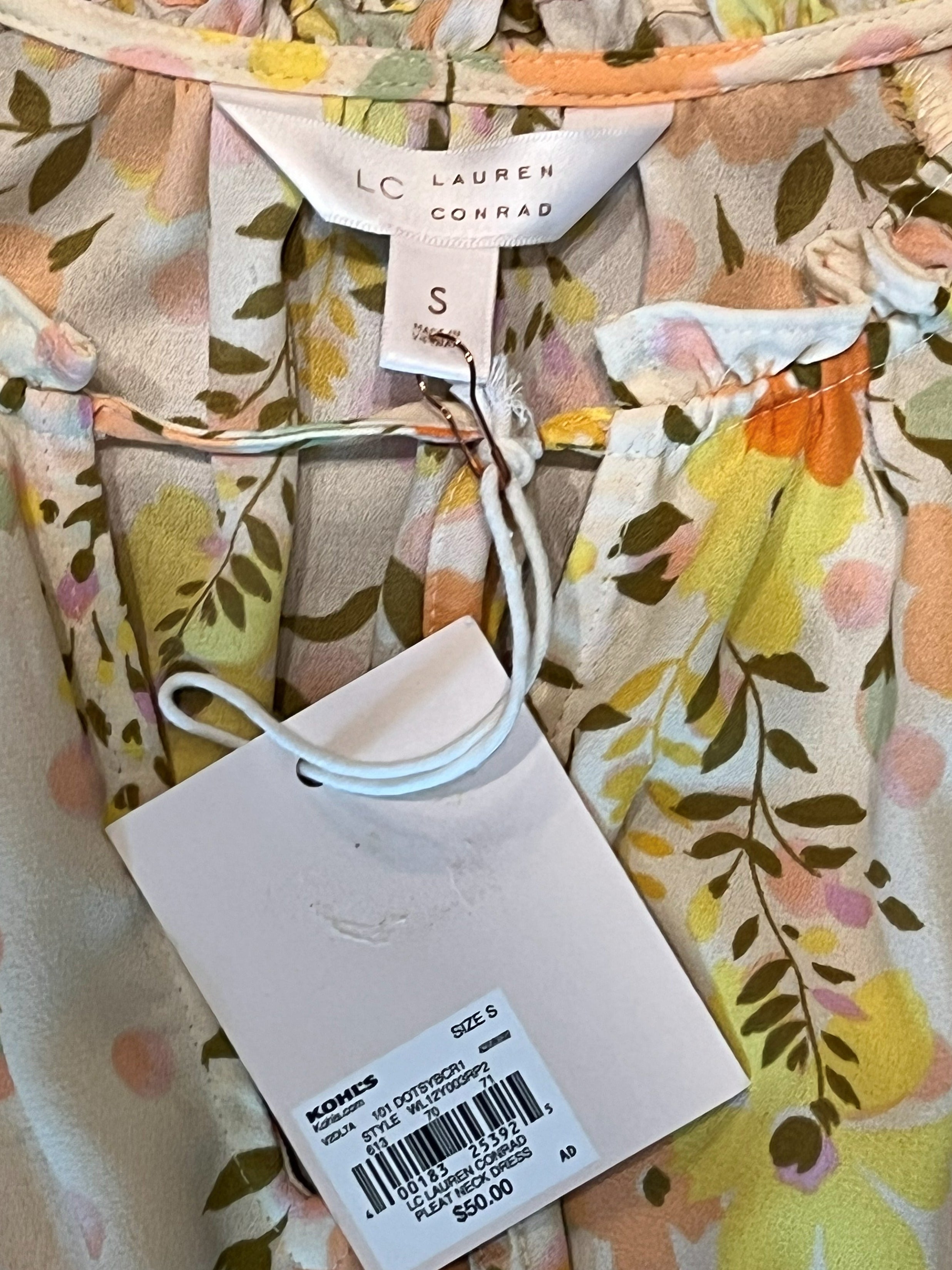A close-up of a Lauren Conrad floral top or dress fabric with a white price tag and size tag attached. The garment features a multicolor floral pattern with yellow, orange, pink, and green on a cream background.