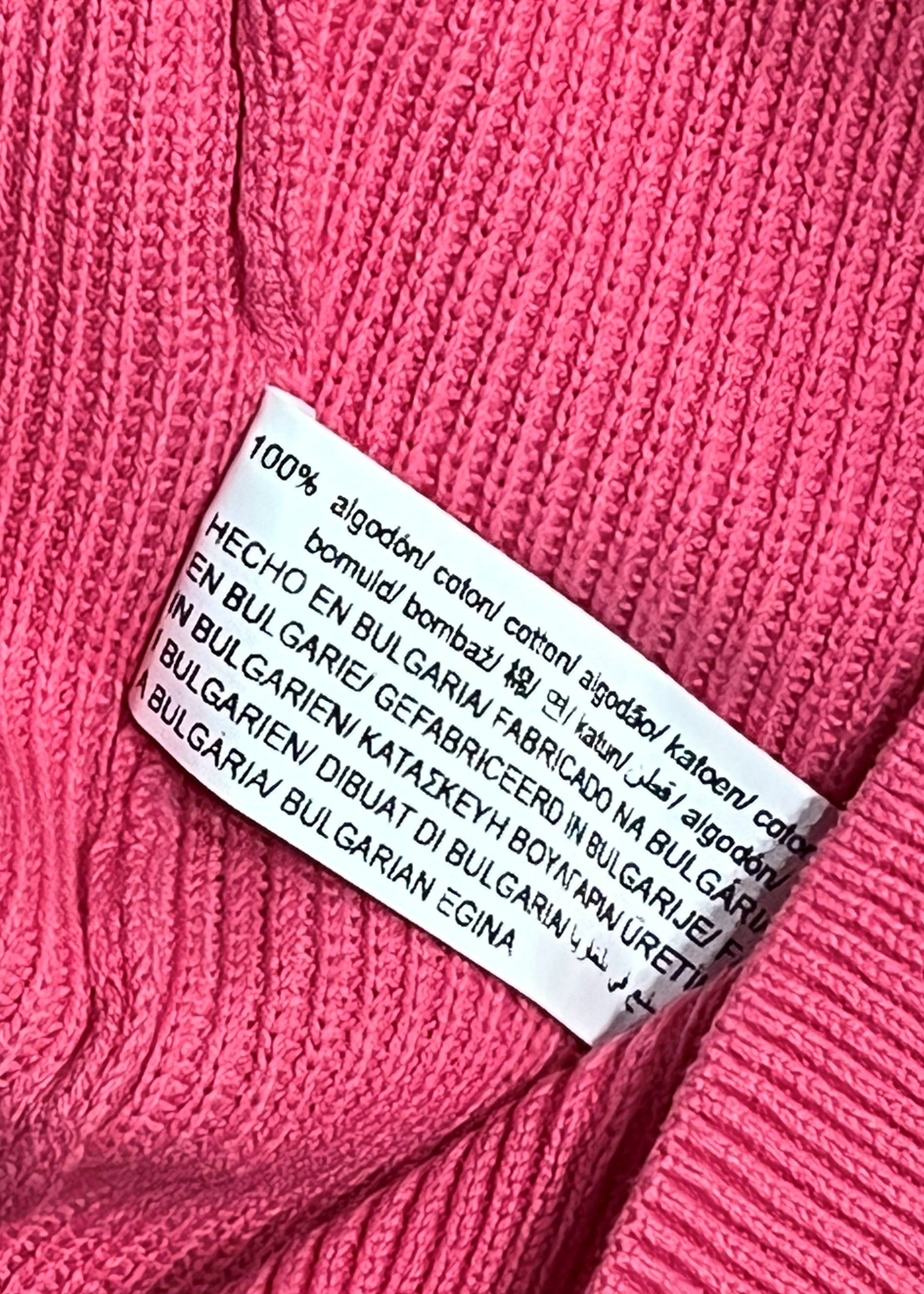 Close-up of a bright pink ribbed knit garment with a white sewn-in care label visible in the center.