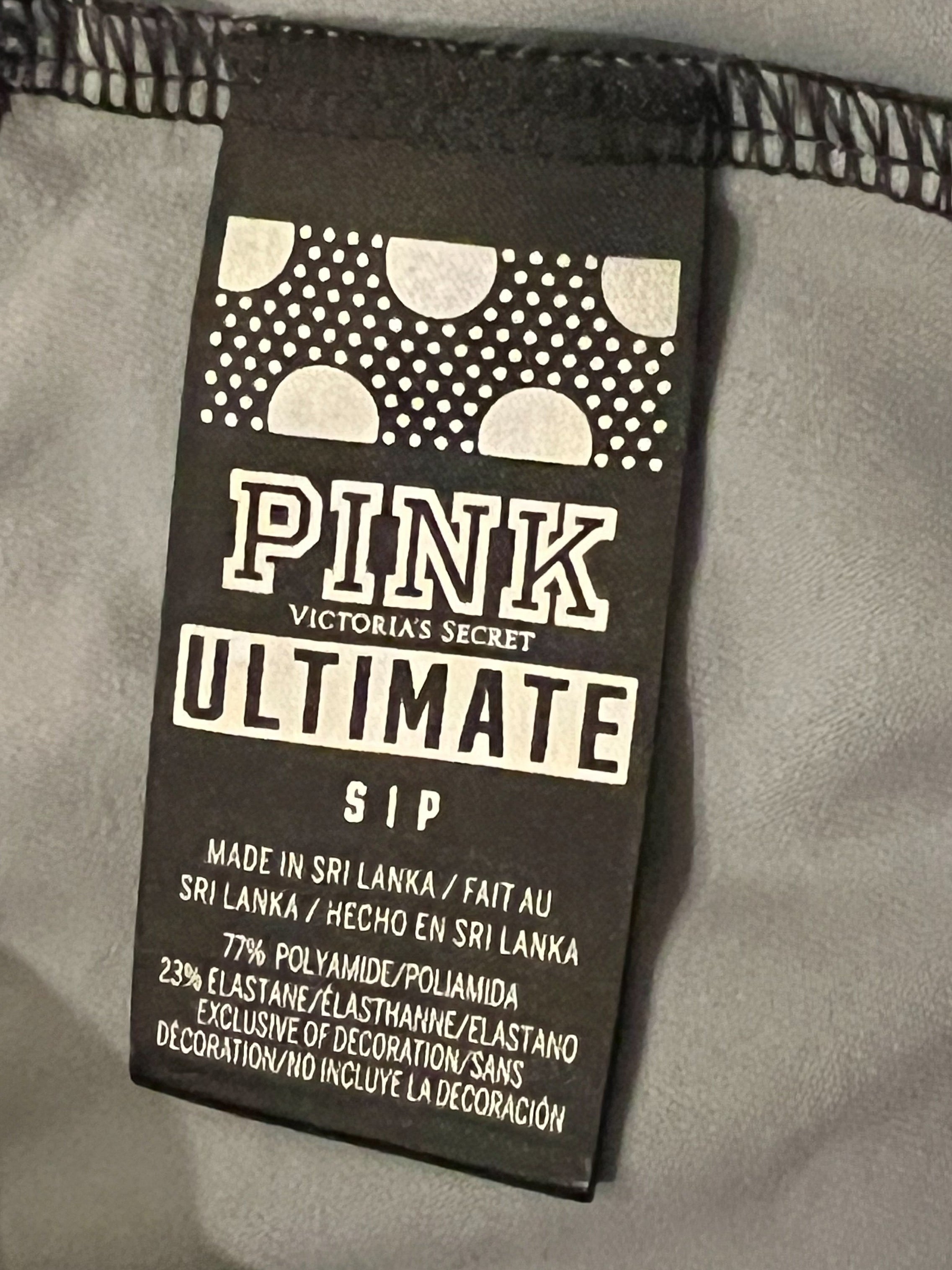 Close-up of a black Victoria's Secret PINK Ultimate slip label sewn onto light gray fabric with black zigzag stitching.