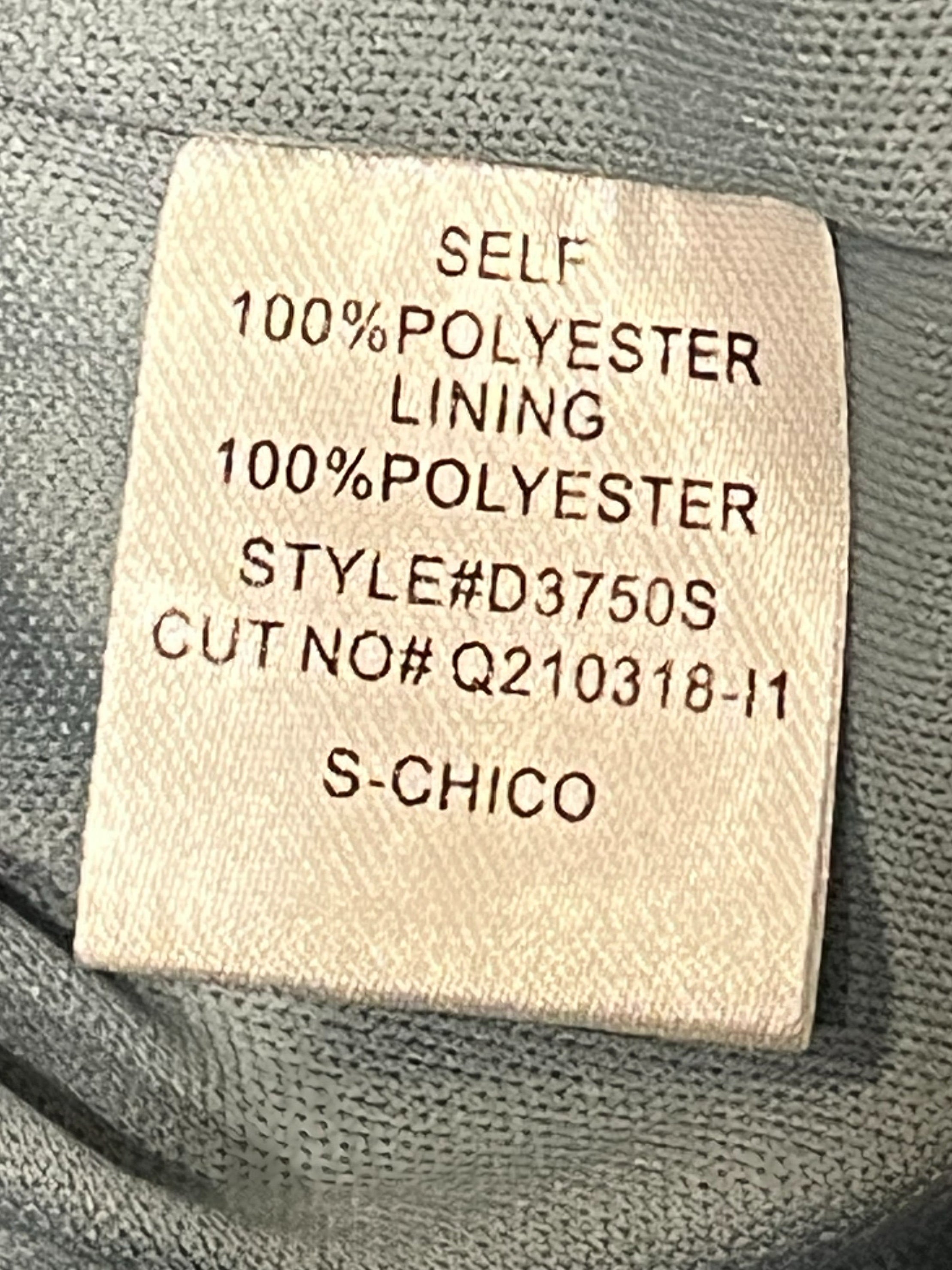 Close-up of a sewn-on fabric label inside a gray knit garment, showing text that reads 'SELF 100% POLYESTER LINING 100% POLYESTER STYLE#D3750S CUT NO# Q210318-11 S-CHICO'.