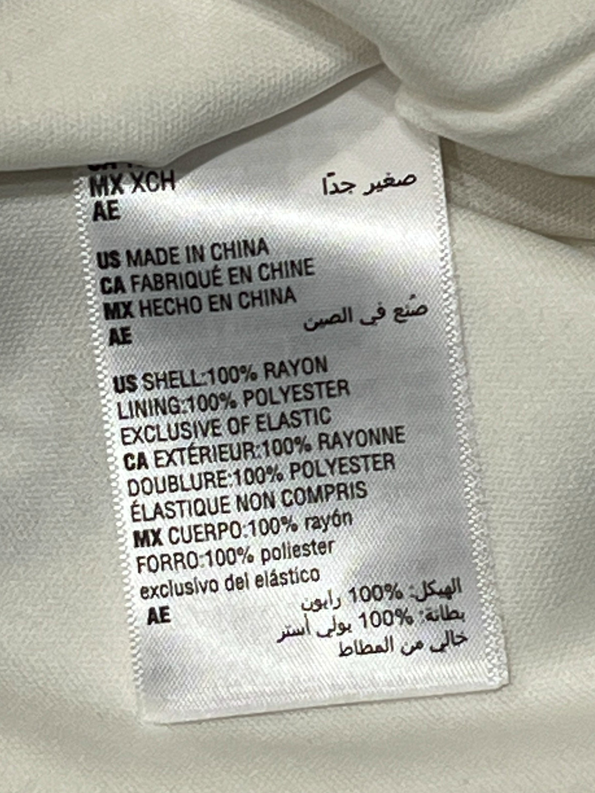 A close-up of a white fabric garment's interior label, showing text including 'MX XOH' and 'MADE IN CHINA' on a white background.