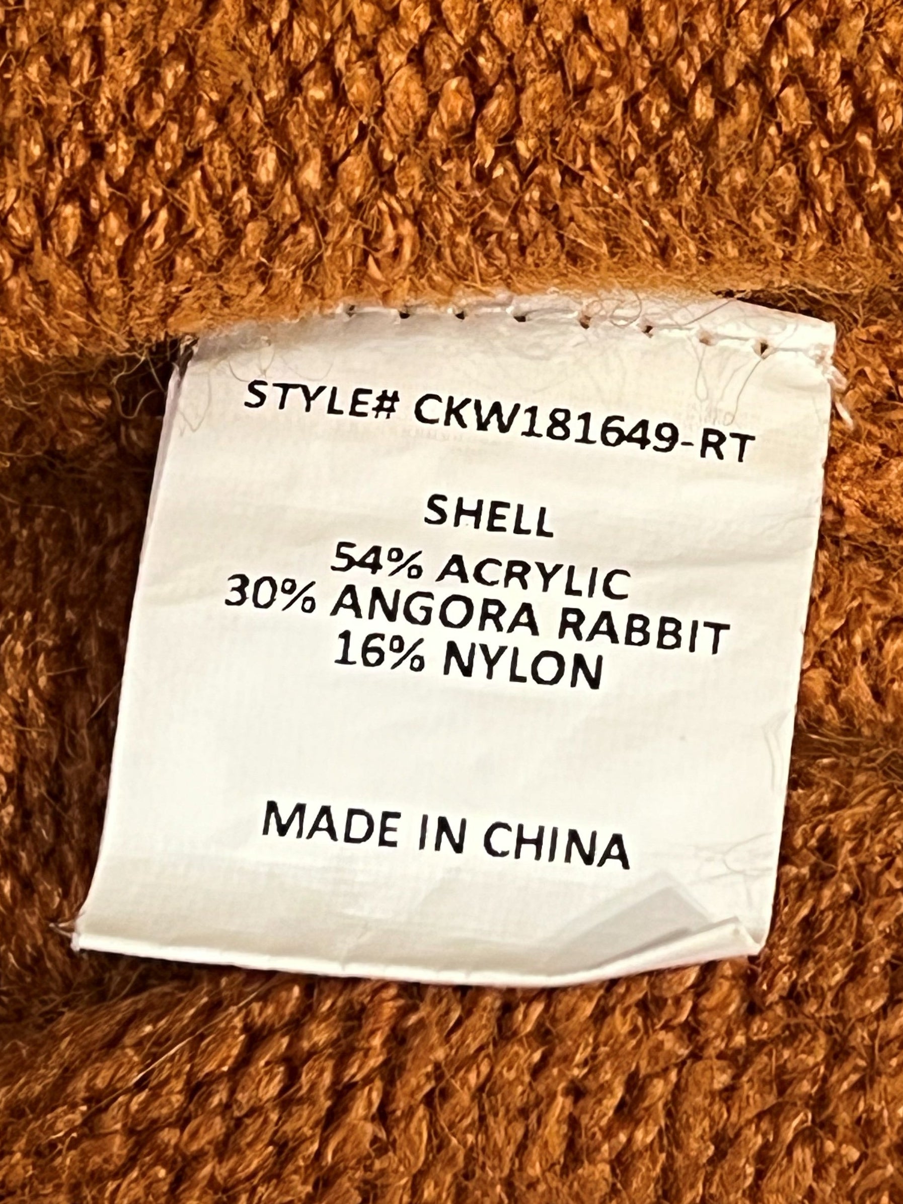 Close-up of a textured orange knit fabric with a white sewn-in product label showing material composition and 'MADE IN CHINA'.