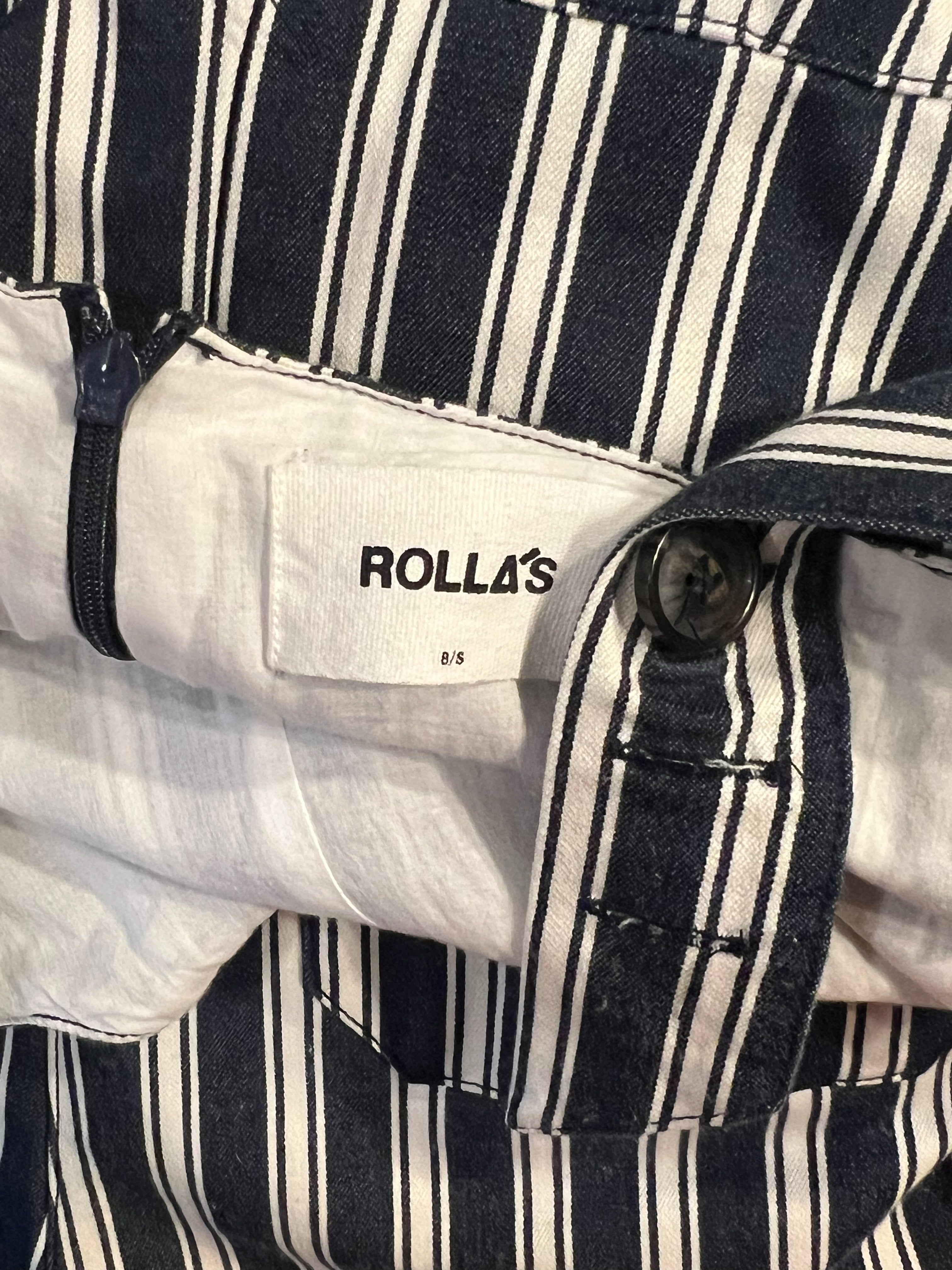 Close-up of striped navy and white trousers showing a button, pocket flap, and a visible ROLLA'S brand label.