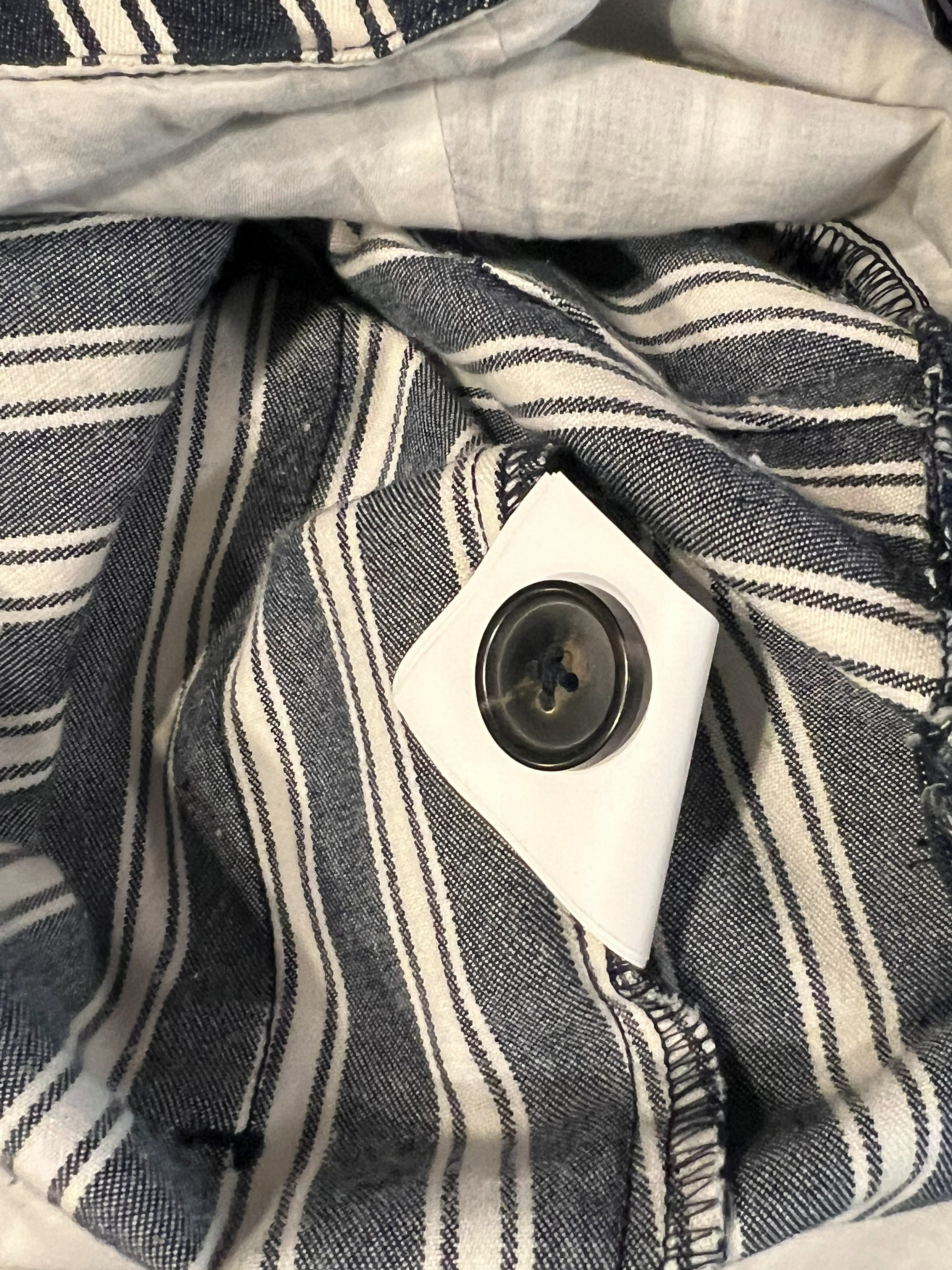 Close-up of a striped fabric garment, likely a shirt or jacket, showing navy and off-white vertical stripes with a white button closure.