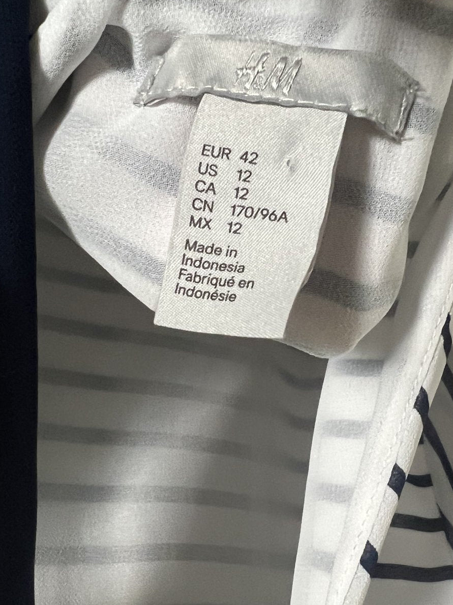 Close-up of a striped garment interior with a visible size tag reading Made in Indonesia and size information. The fabric is white with dark navy horizontal stripes, and a hand is holding the garment open.