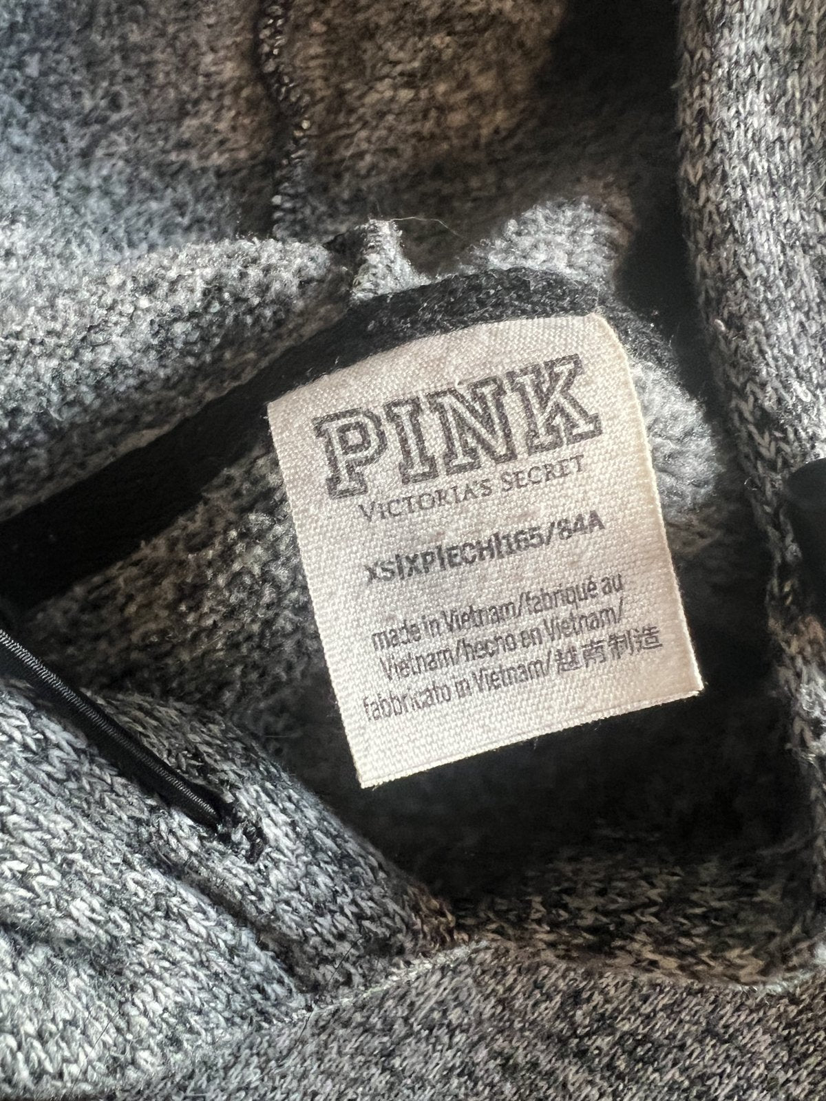 Close-up of a gray and black heathered knit garment label reading PINK Victoria's Secret, with the brand name and size information visible.