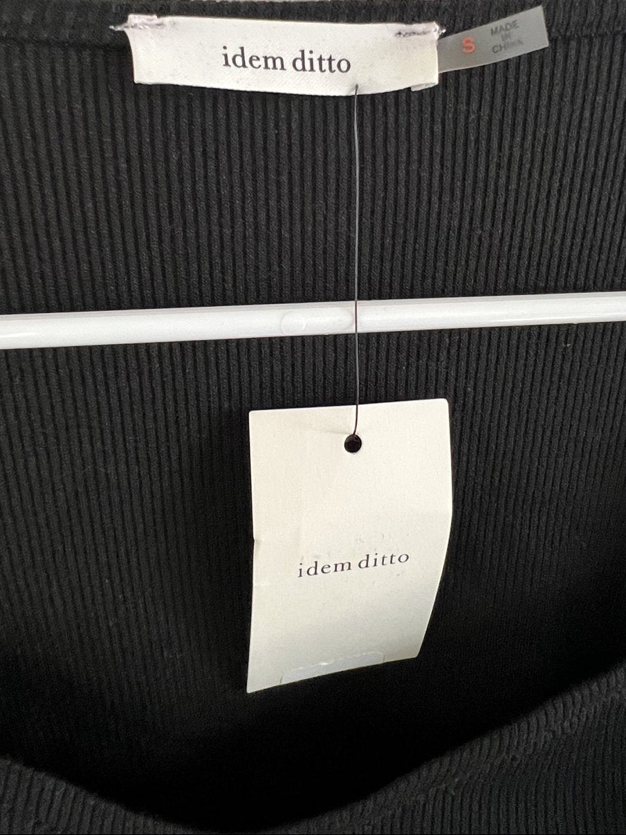 Close-up of a black ribbed knit garment hanging on a white hanger, with an 'idem ditto' brand label and paper tag visible