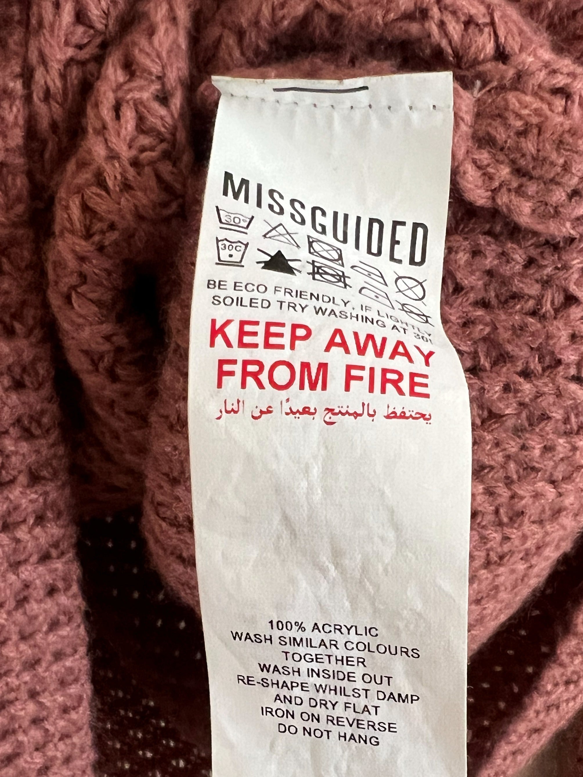 A close-up of a dusty rose pink chunky knit sweater with a prominent white Missguided care label attached.