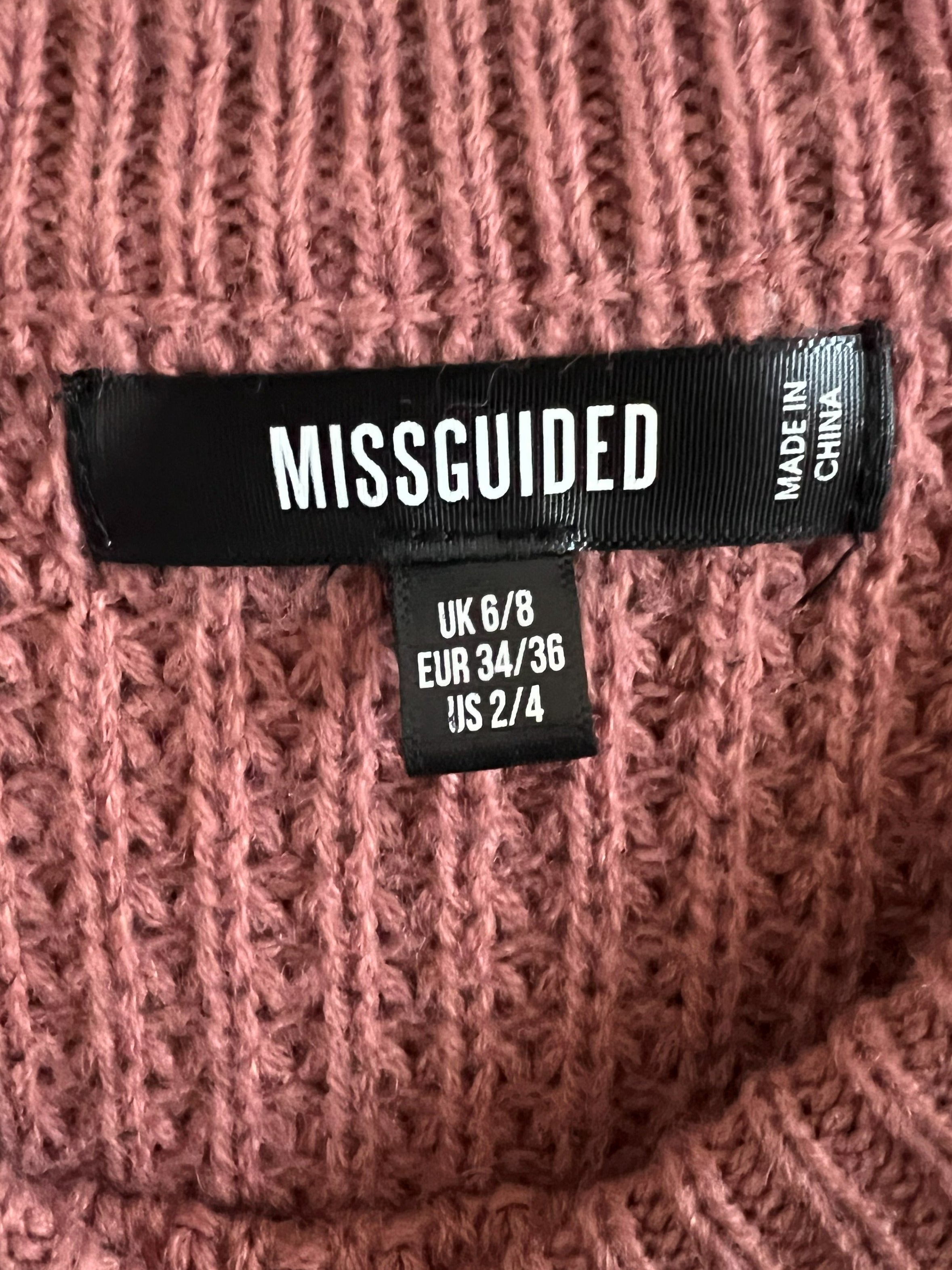 Close-up of a ribbed knit sweater in dusty rose pink, showing a black MISSGUIDED brand label and size tag.