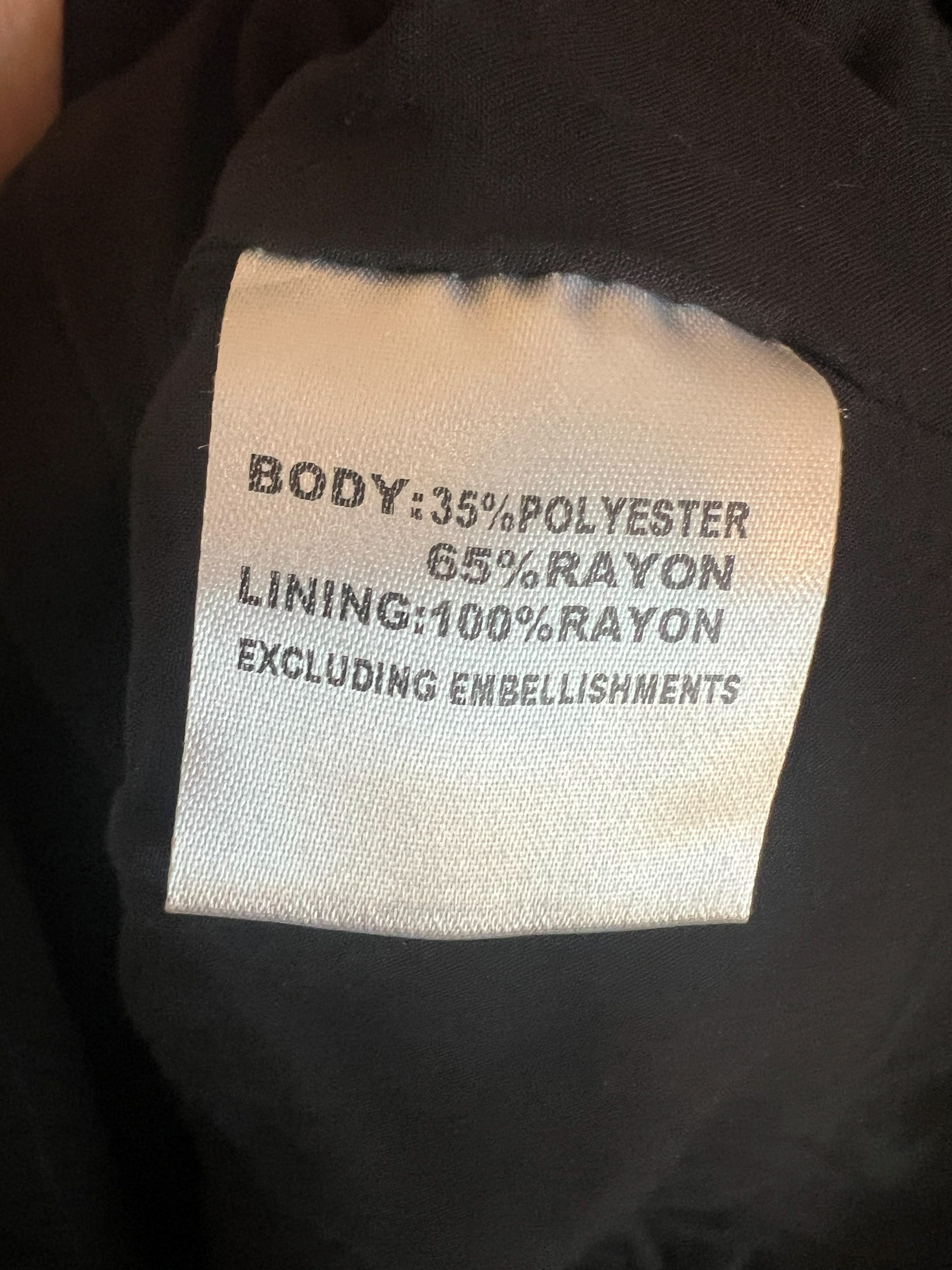 Close-up of a garment's interior label showing fabric composition: 35% polyester, 65% rayon, and 100% rayon lining, with black fabric surrounding the white label.