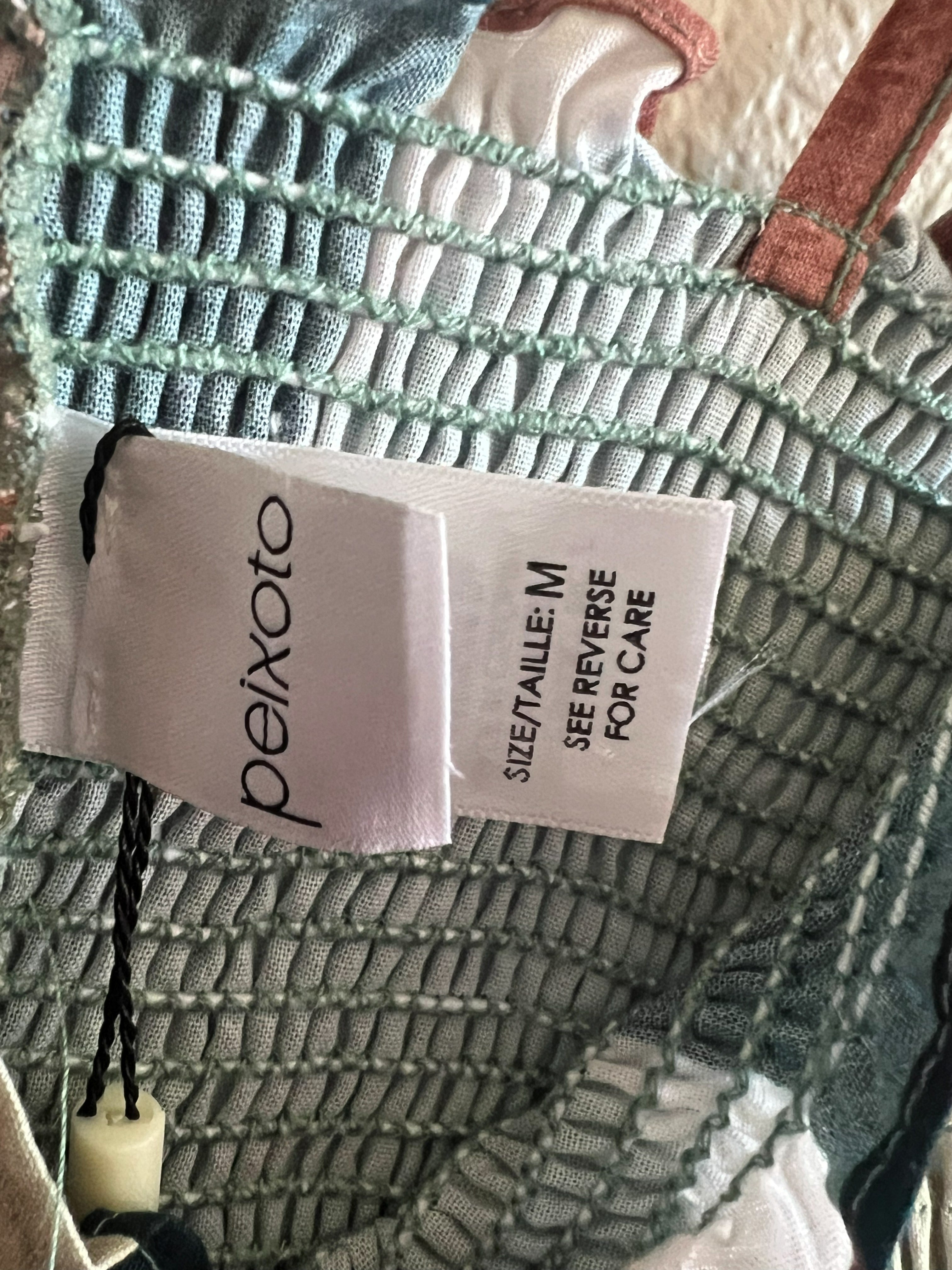 Close-up of a garment's smocked mesh interior showing a white Peixoto brand tag with size M and care instructions.