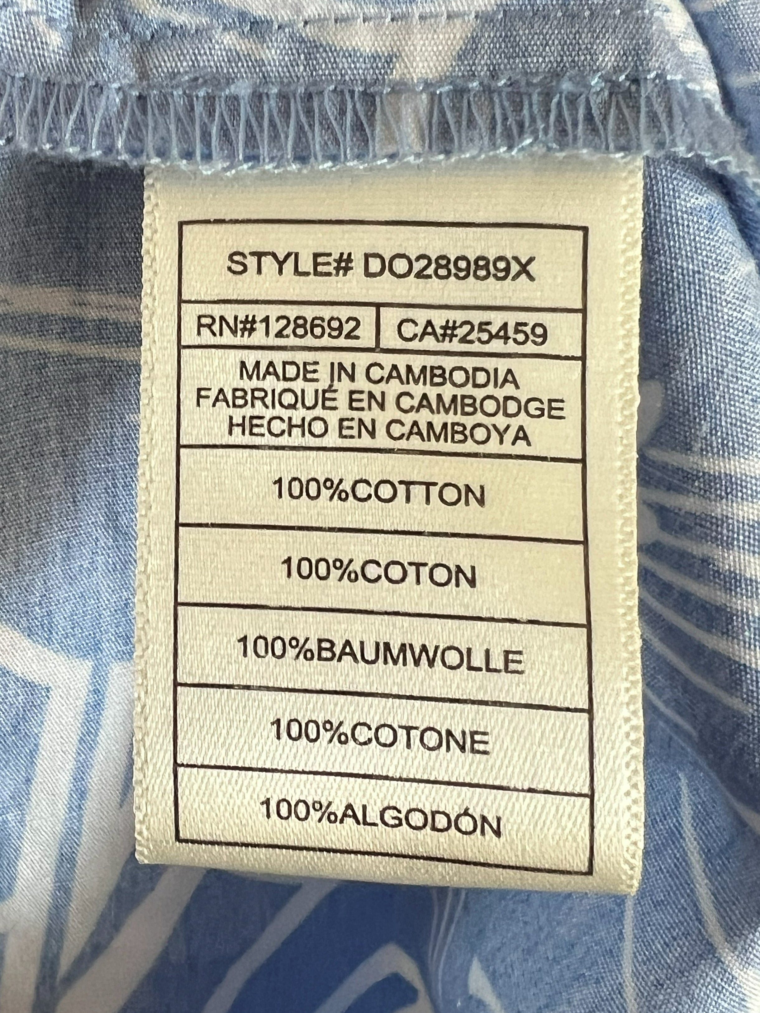 Close-up of a fabric care label sewn onto a light blue and white patterned garment, showing text including '100% COTTON' and 'MADE IN CAMBODIA'.