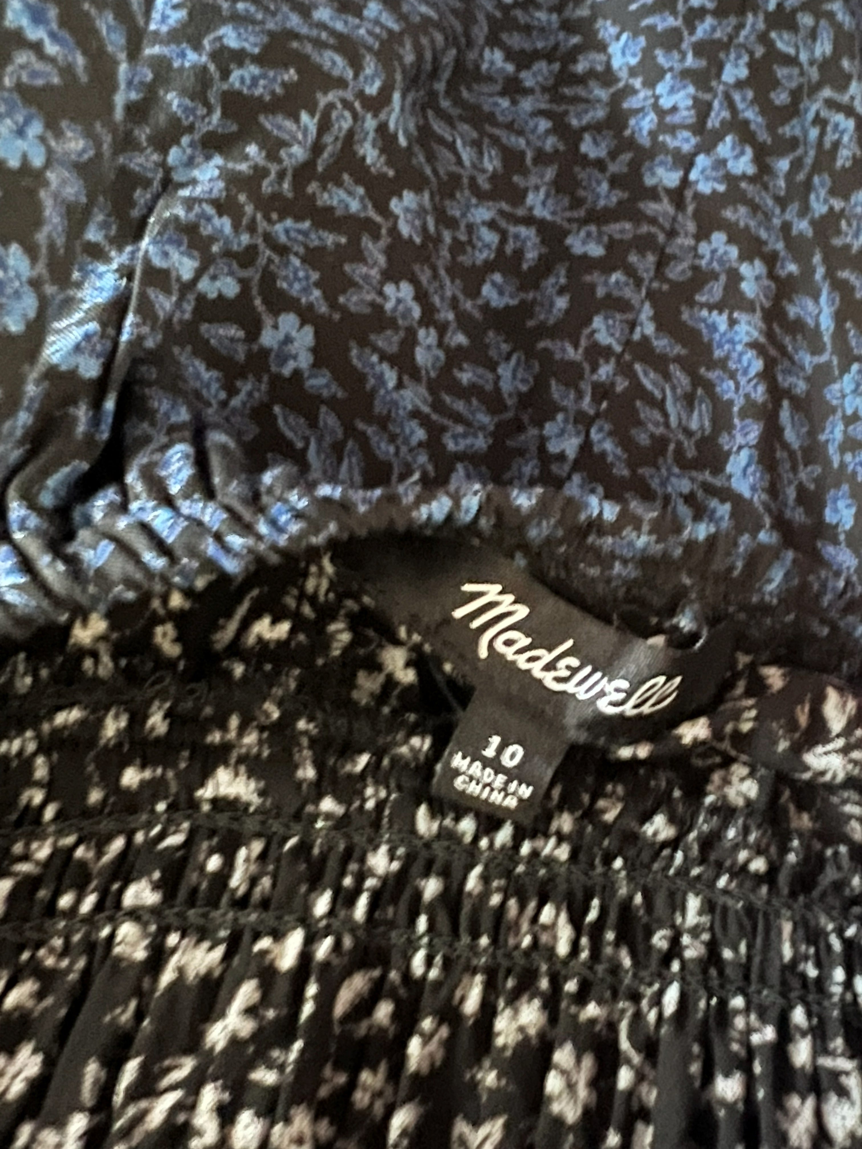 Close-up of a garment waistband showing a black and white floral print on the upper section and a black and blue floral print on the lower section, with a sewn-in size tag reading Medford 06.