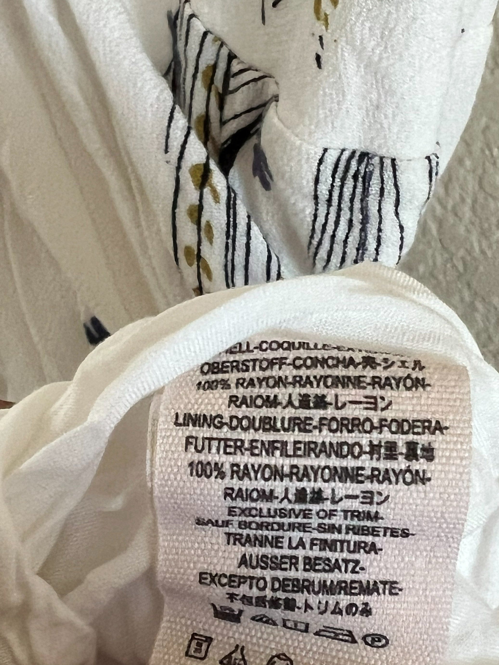 Close-up of a garment's inner care label  showing text for RAIOM and fabric care symbols on white fabric.