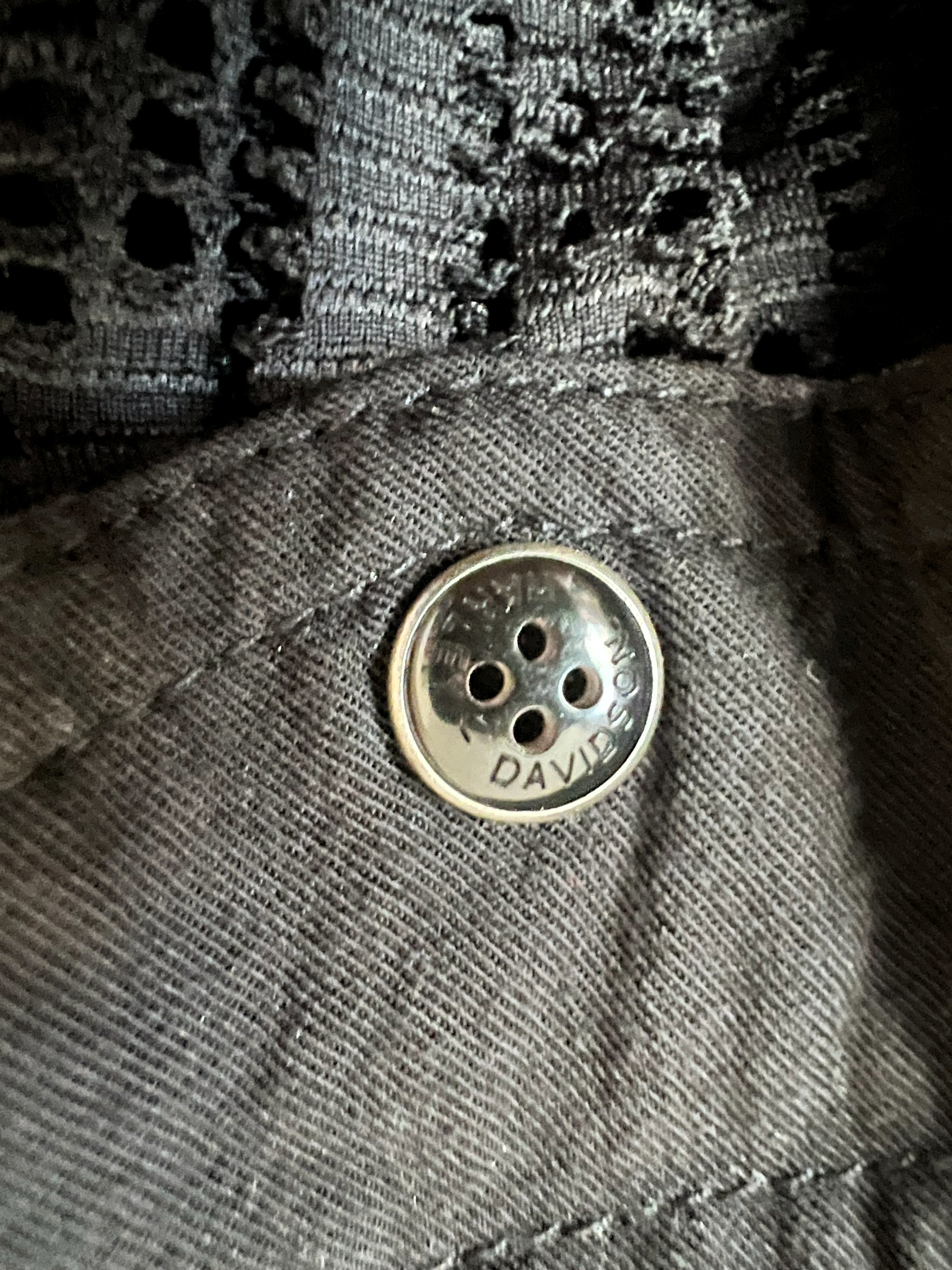 Close-up of a dark gray denim fabric with a silver metal button engraved with the brand name 'Harley Davidson'.