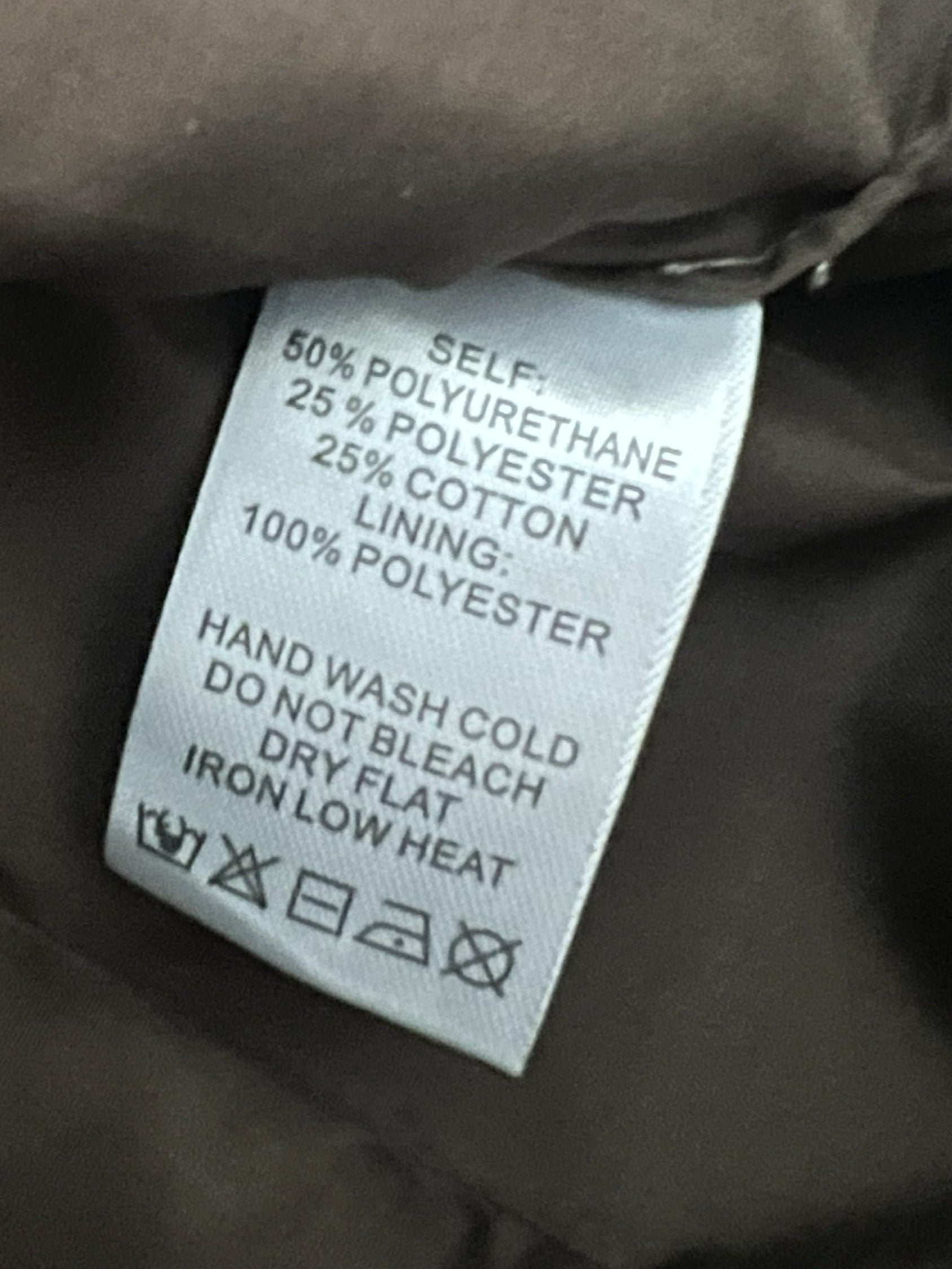 Close-up of a garment's interior label showing fabric composition and care instructions, photographed against dark brown or black fabric.