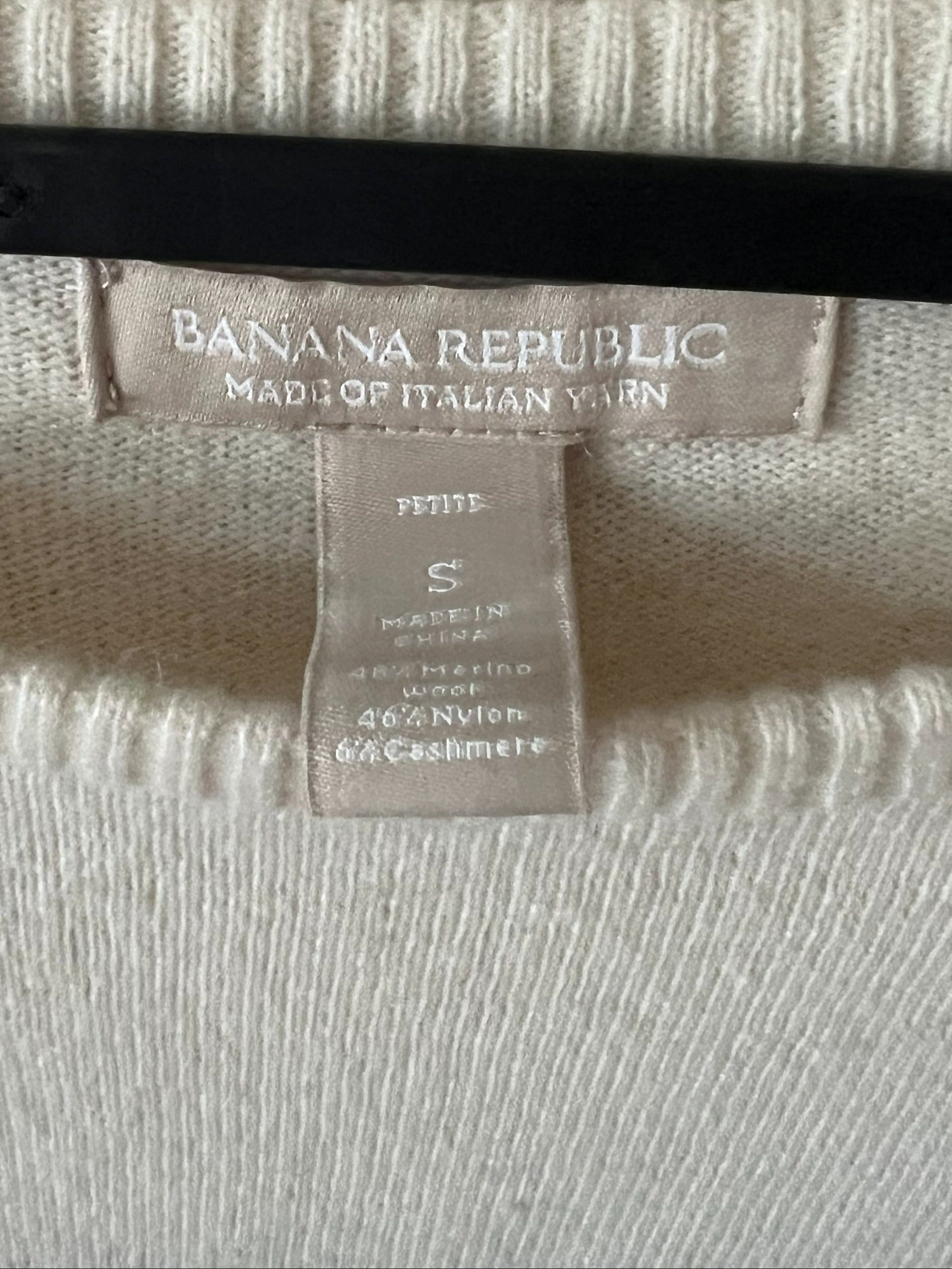 Close-up of a cream-colored knit sweater with a ribbed collar, featuring a visible Banana Republic brand label and a size tag.
