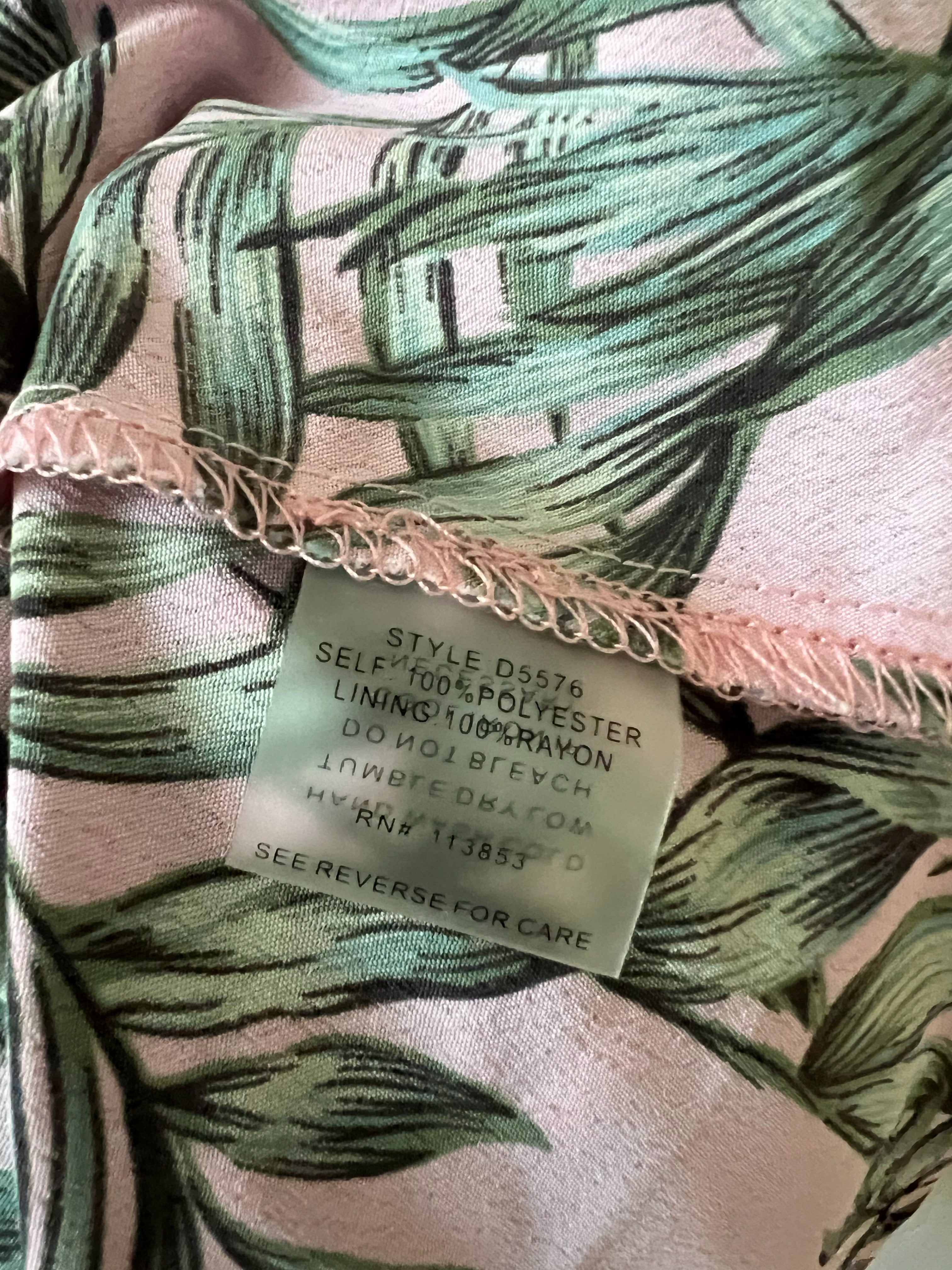 Close-up of a pink and green tropical leaf patterned fabric with a visible sewn-in care label reading 'STYLE DS576 SELF-ASSEMBLY POLYESTER LININGS 100% RAWON'.