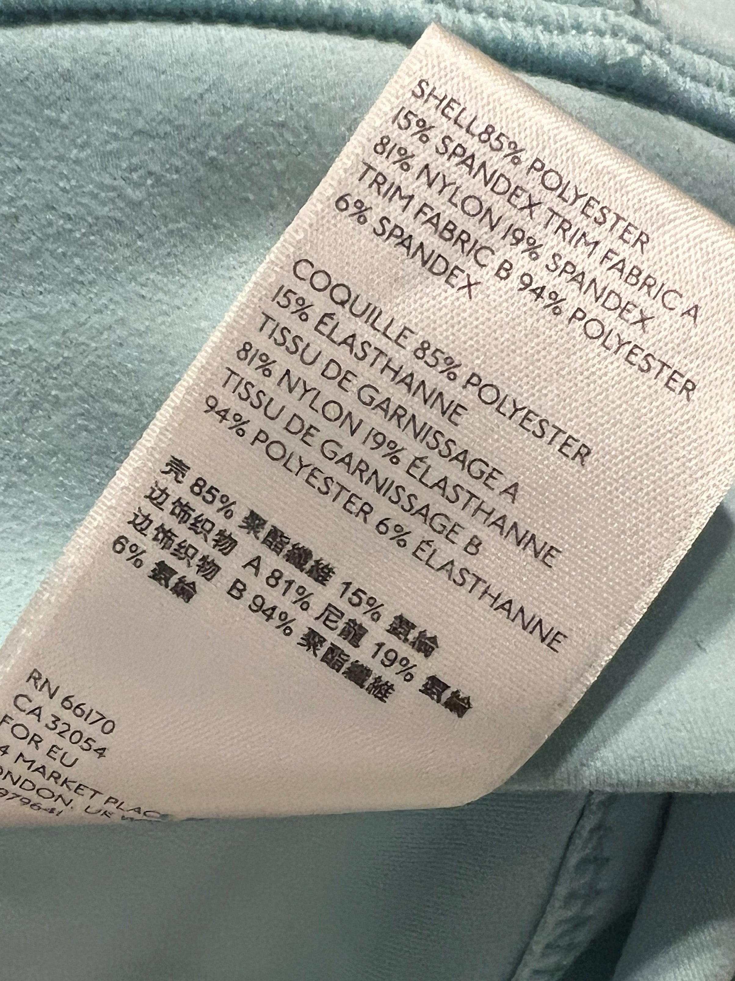 Close-up of a garment's fabric tag showing material composition in English and Chinese, with the surrounding light blue textile visible.