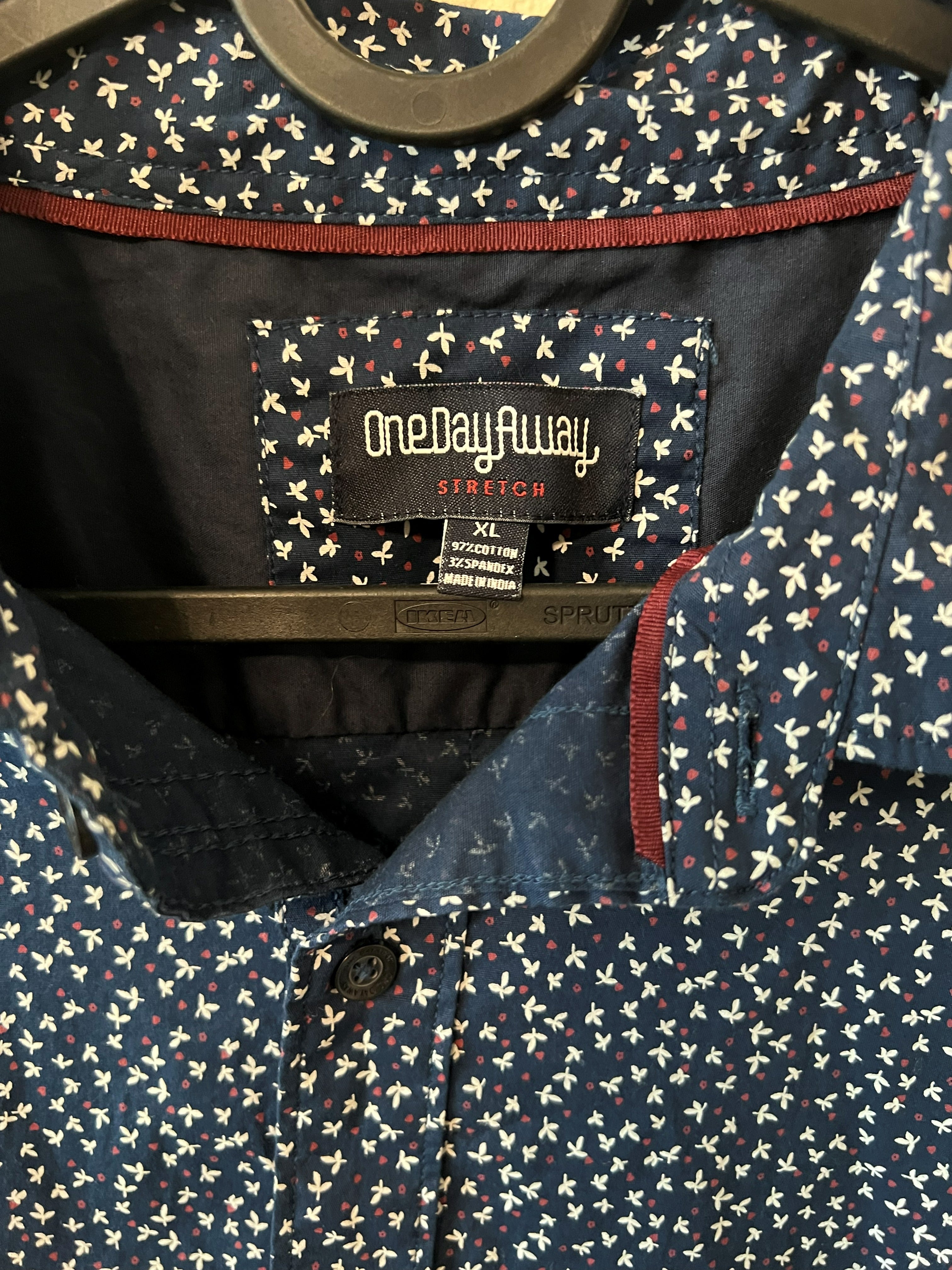 Close-up of a patterned collared shirt with a visible OneDayAway Stretch brand label. The fabric is navy blue with a dense small-scale white and red pattern, featuring a dark navy inner collar lining with a red stitched border.
