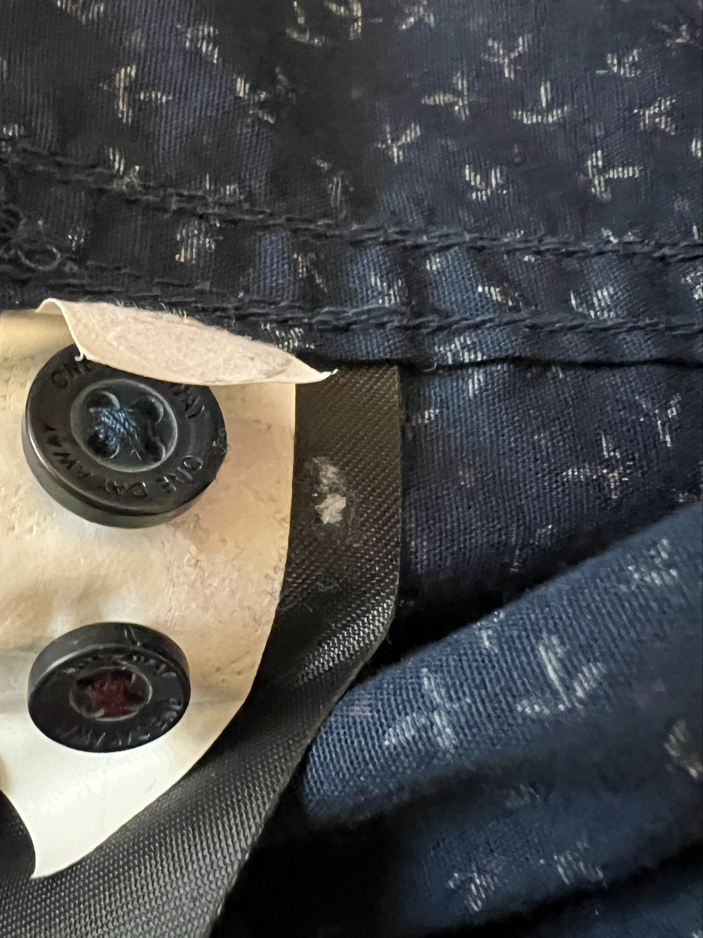 Close-up of a dark navy patterned fabric garment with a black button and a piece of white paper covering it.