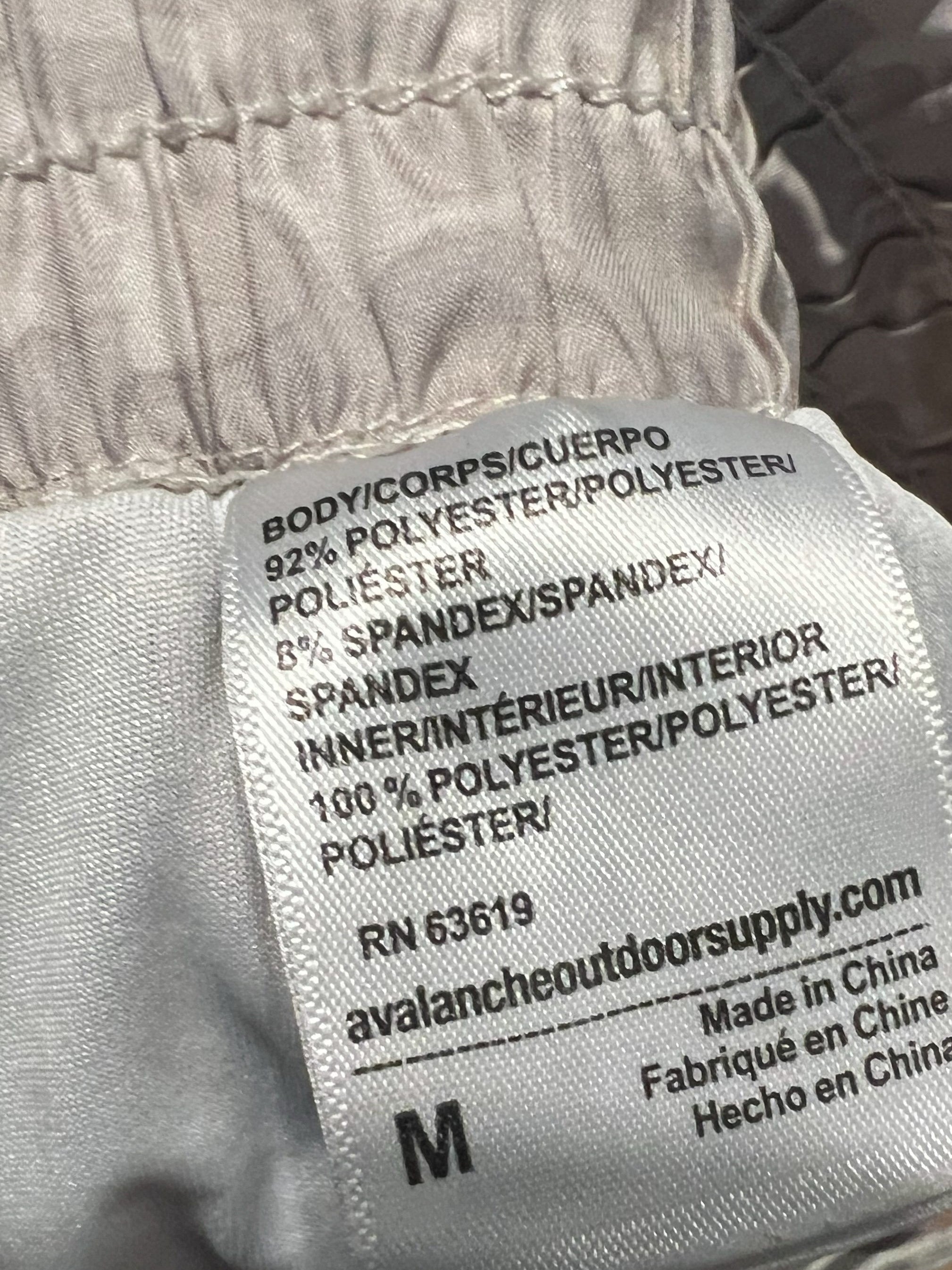 Close-up of a gray fabric garment with a sewn-in care label showing text including 'bodycon poliesterguiero', 'SPANDEX TRIEURINTER', 'Made in China', and size 'M'.