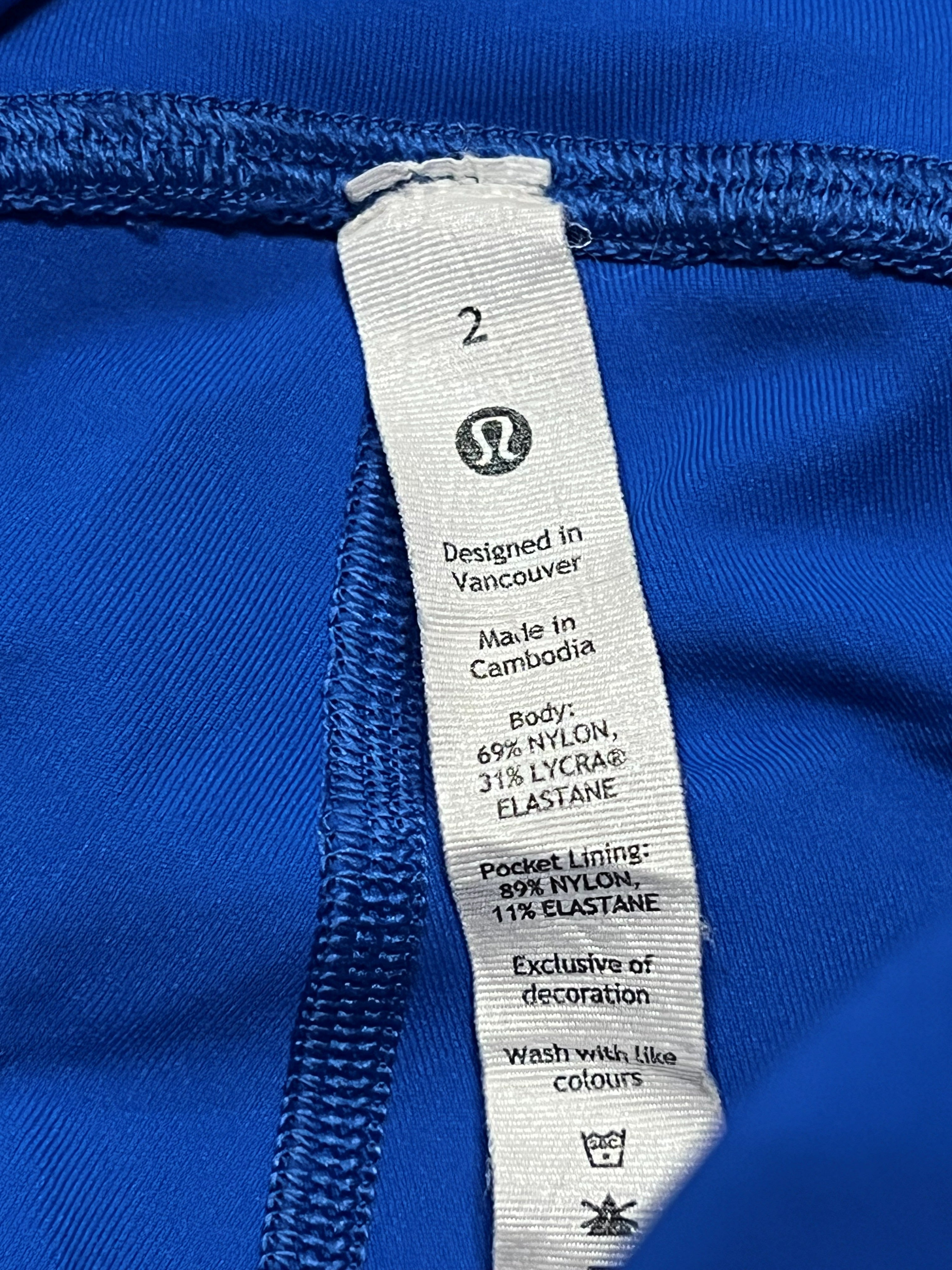 Close-up of a white Lululemon garment care label sewn onto a bright royal blue fabric, showing size 2 and material details.