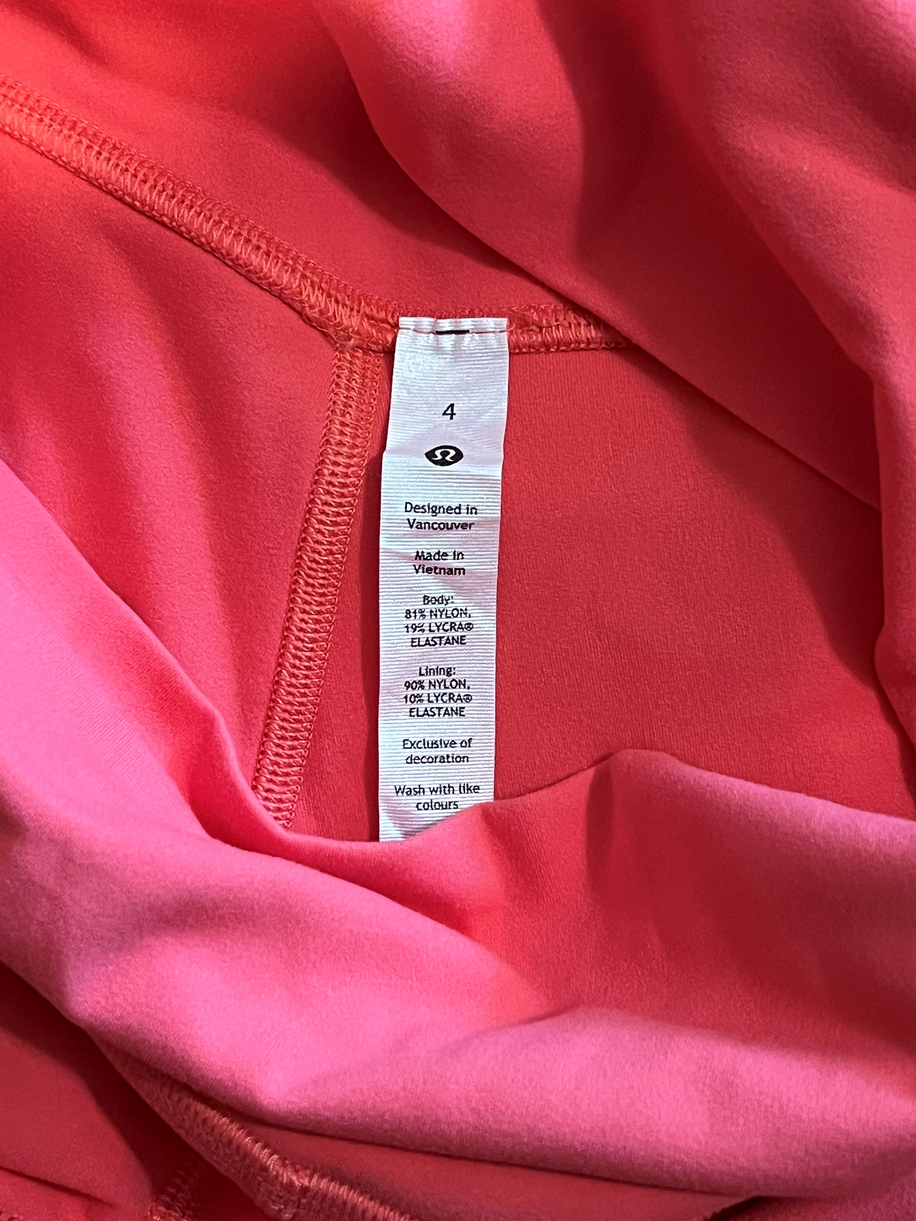 Close-up of a coral pink athletic top showing the inner neck label, with ribbed knit fabric and a white size tag reading 4.