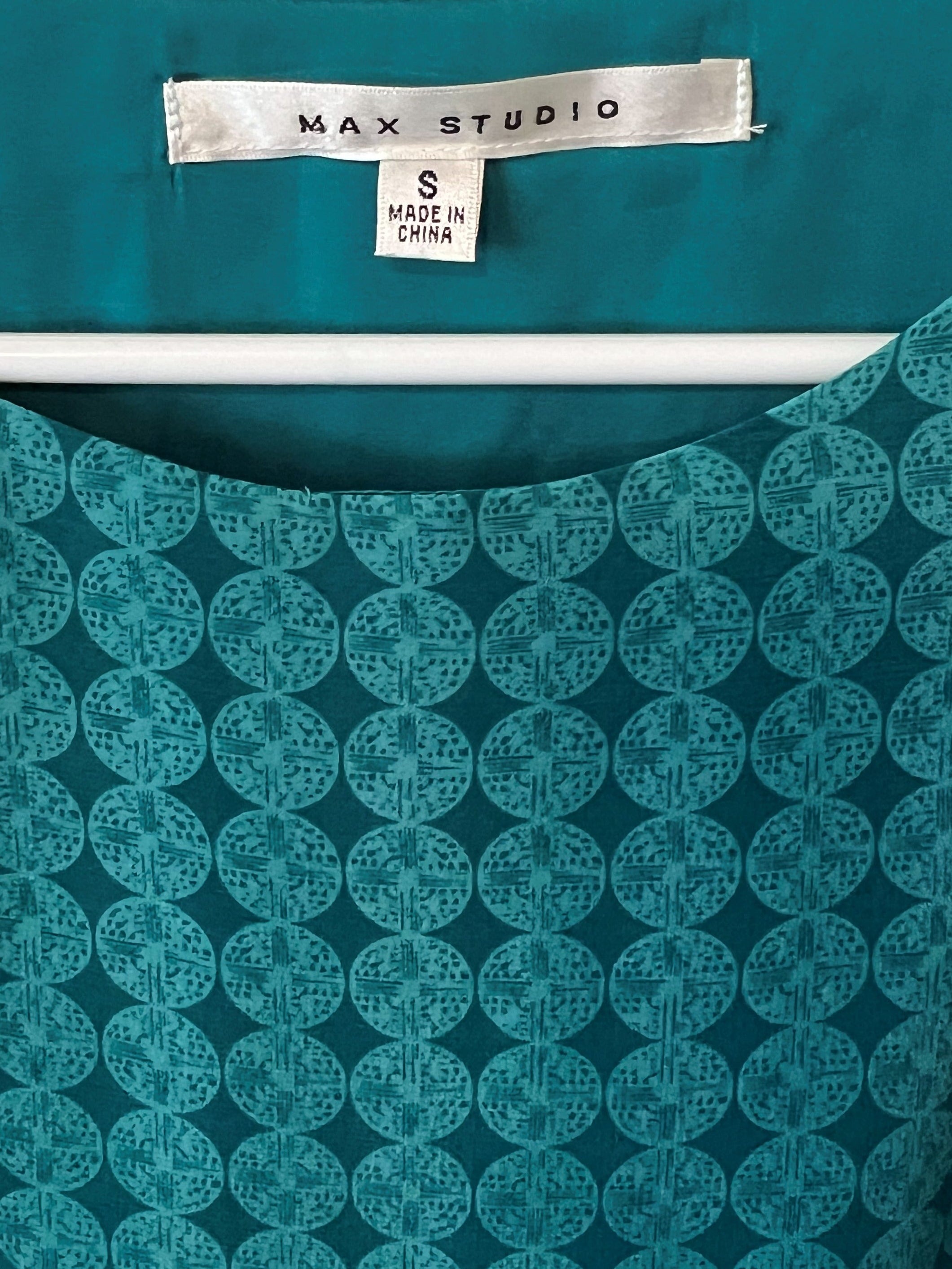 A close-up of a teal patterned dress. The brand label 'MAX STUDIO' is visible at the neckline.