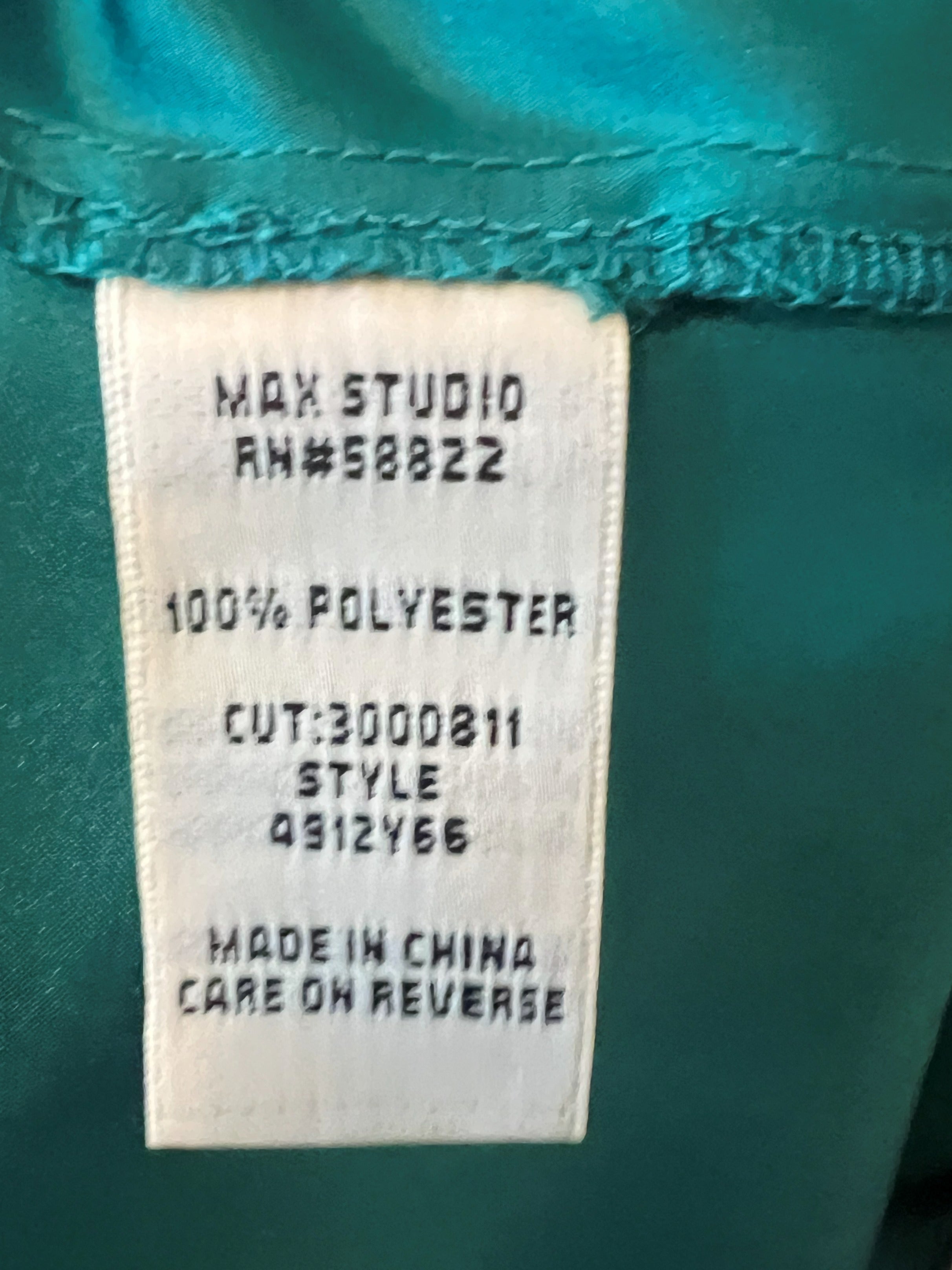 Close-up of a garment's interior label reading 'MAX STUDIO RN#58822', '100% POLYESTER', 'CUT:3000811 STYLE 4912Y66', and 'MADE IN CHINA CARE ON REVERSE', attached to teal fabric.