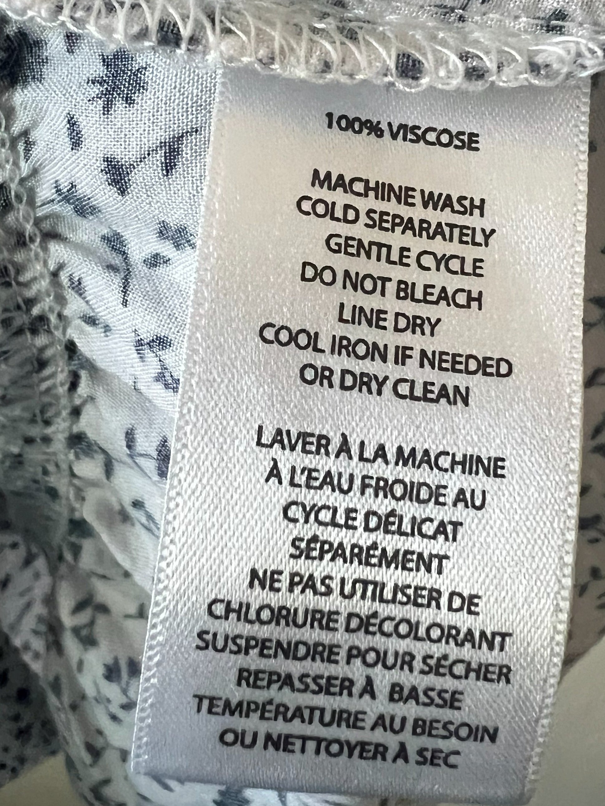 Close-up of a garment's interior neck label reading '100% VISCOS' with care instructions, surrounded by white fabric with a small dark blue floral print.