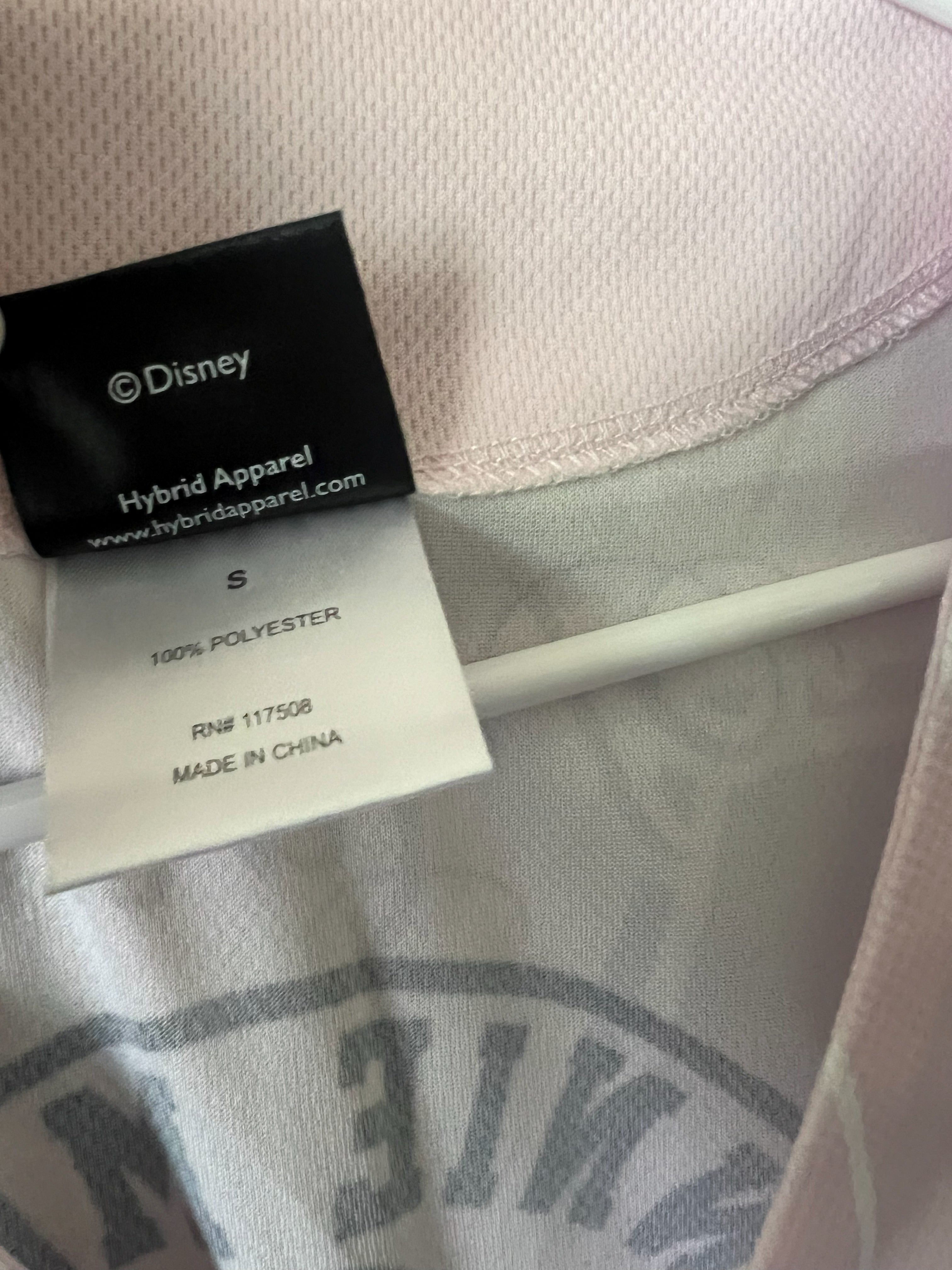 Close-up of a Disney Hybrid Apparel garment tag on a light pink and white fabric item, showing the brand name Disney and size S.
