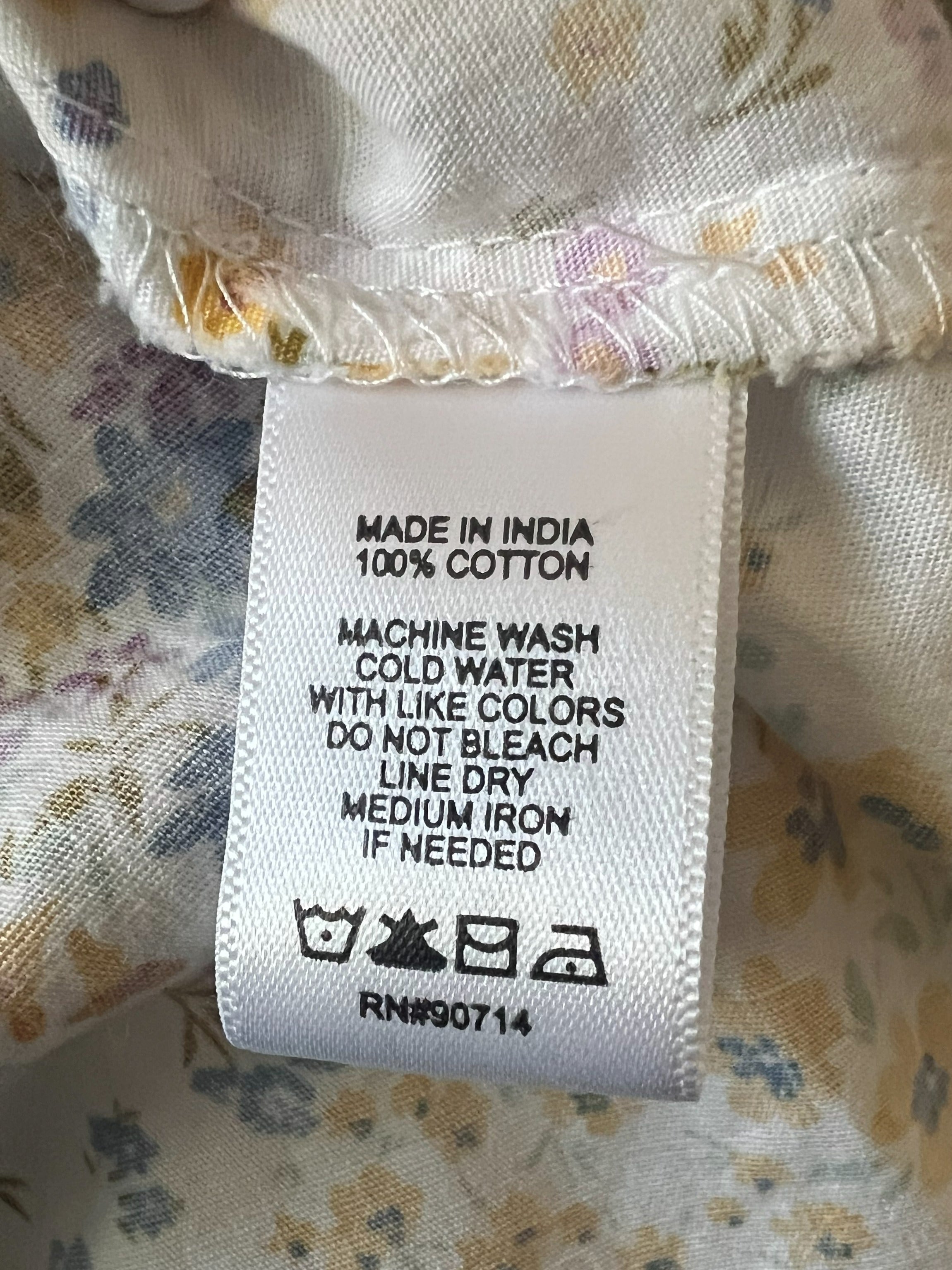 Close-up of a floral-patterned garment label showing care instructions and text including 'MADE IN INDIA 100% COTTON'.