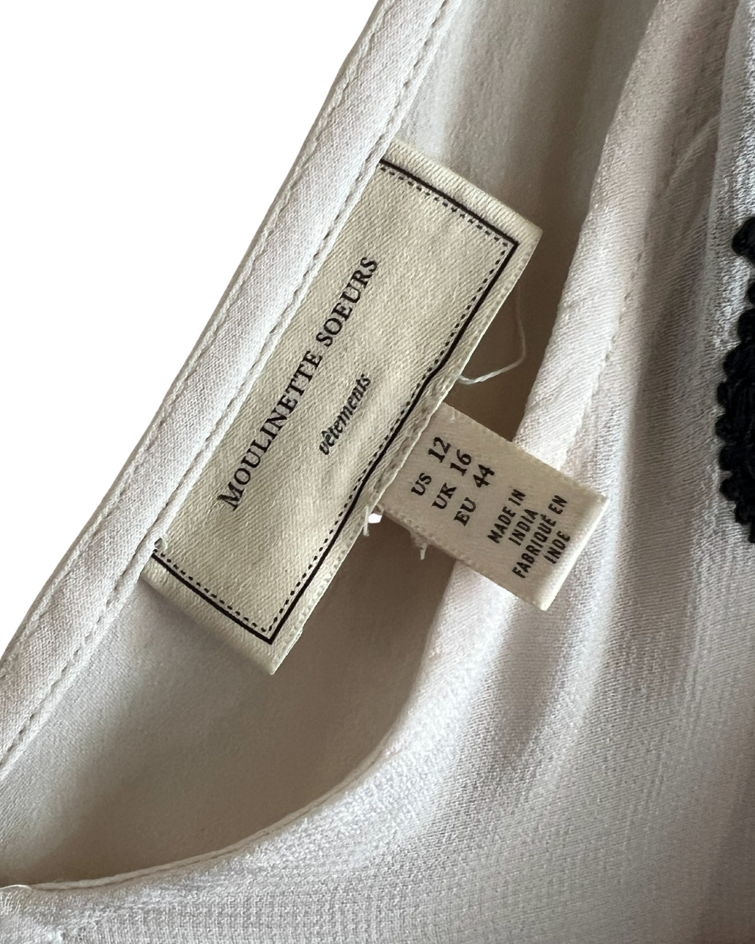 Close-up of a white or off-white fabric garment showing interior labels, including a sewn-in label reading 'MOULINETTE SOEURS' and a size tag.