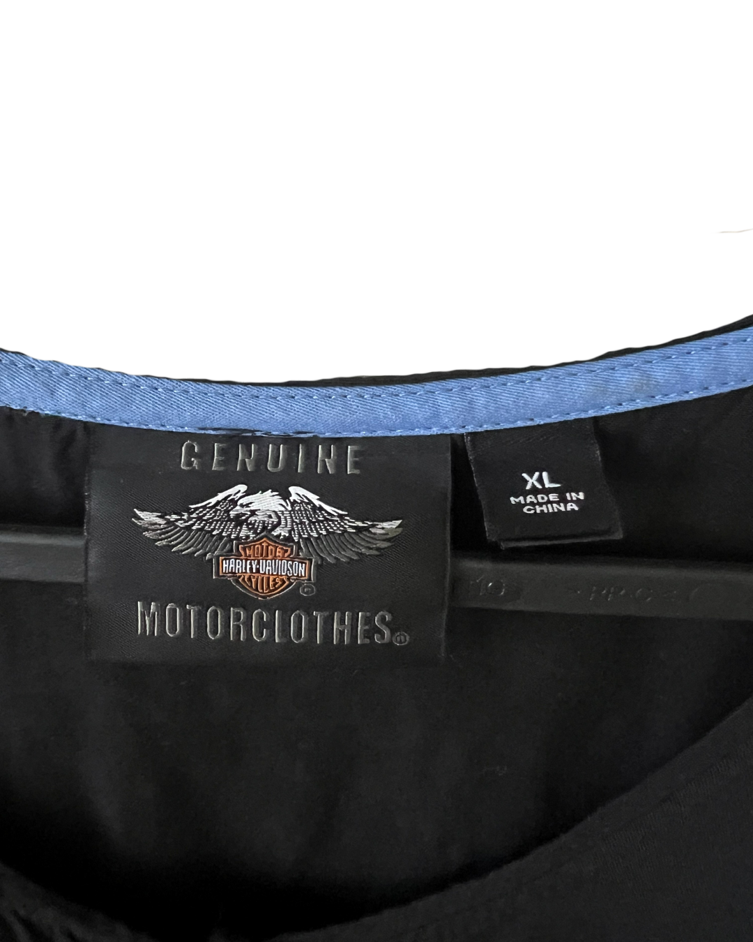 Close-up of the inner neck area of a black garment, showing a Harley-Davidson Motorclothes 'Genuine' label, a size 'XL' tag, and a blue inner lining.