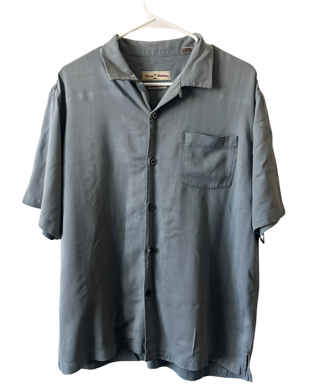 A short-sleeve button-up shirt in a muted slate blue-gray color, hanging on a white plastic hanger against a plain white background. The shirt features a classic collar, dark buttons, and a single chest pocket.