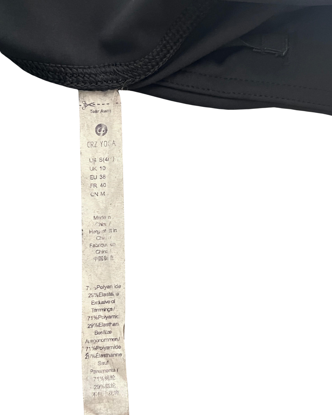 A close-up of a black fabric item showing a sewn-on paper tag with the brand name Cruz Yoga and country of origin details, set against a plain white background.