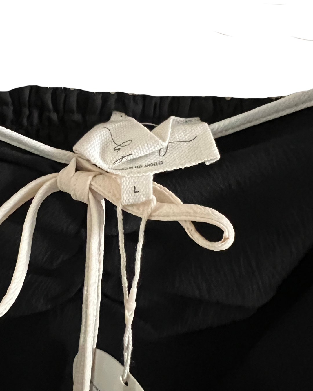 Close-up of black drawstring shorts with a cream-colored woven brand tag and tie, showing the size 'L'.