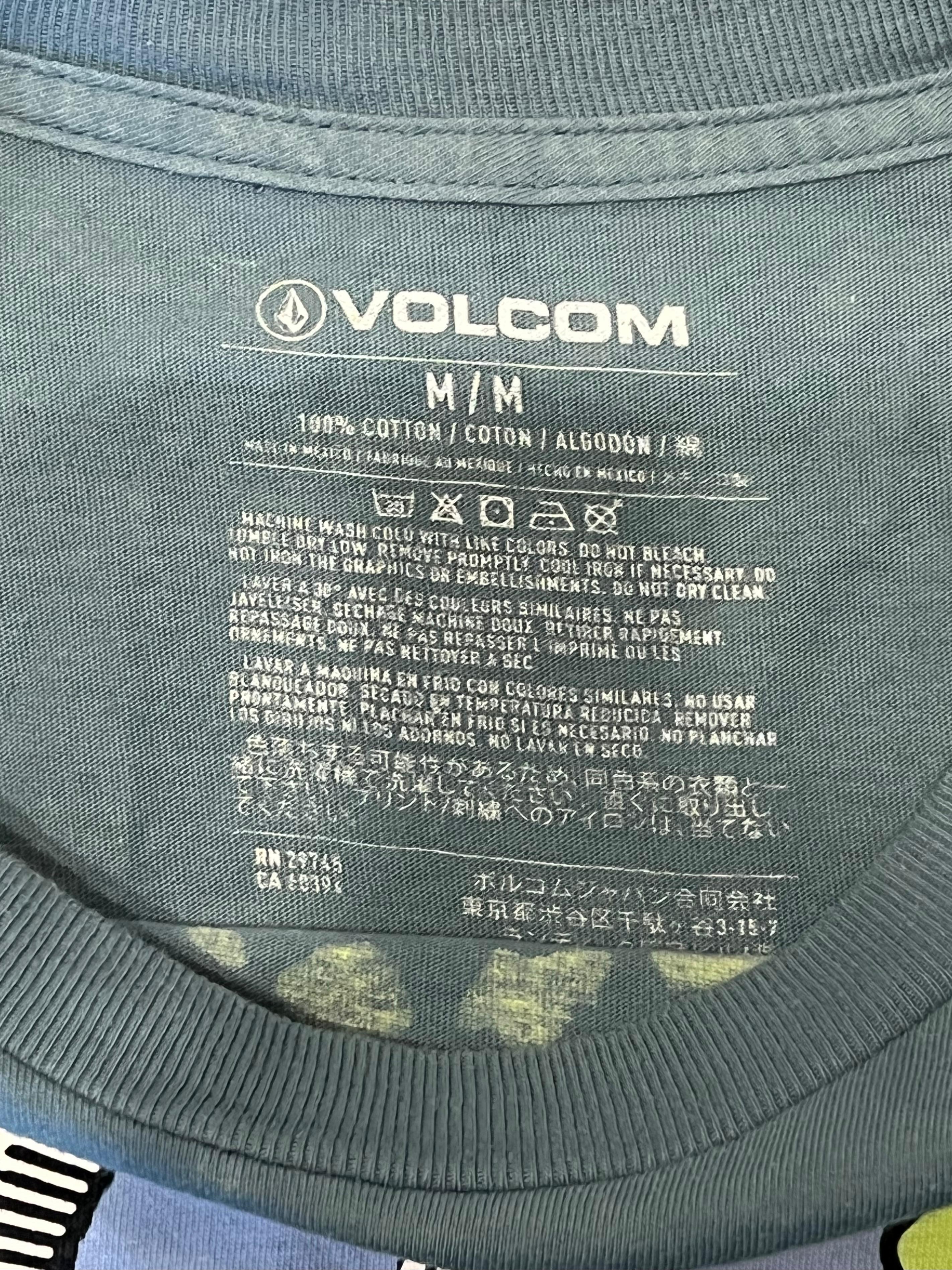 Close-up of the inside collar of a dark gray Volcom t-shirt, showing the printed Volcom logo, size 'M/M', and care instructions.